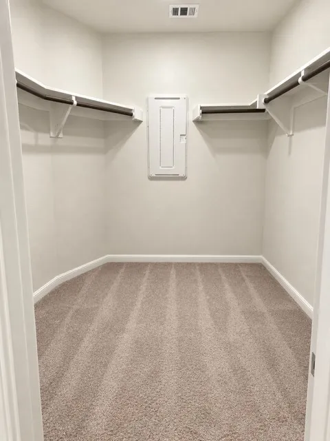 Walk-in closet with carpet flooring, white shelving, and hanging rods