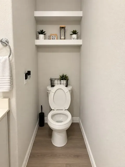 Wood-finish flooring with white baseboards, a white toilet, and built-in floating shelves