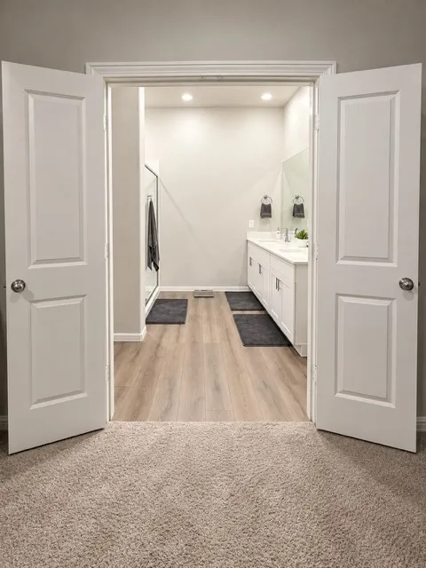 Double doors open to a bathroom featuring wood-finish flooring, a double vanity with two sinks, and integrated ceiling lighting