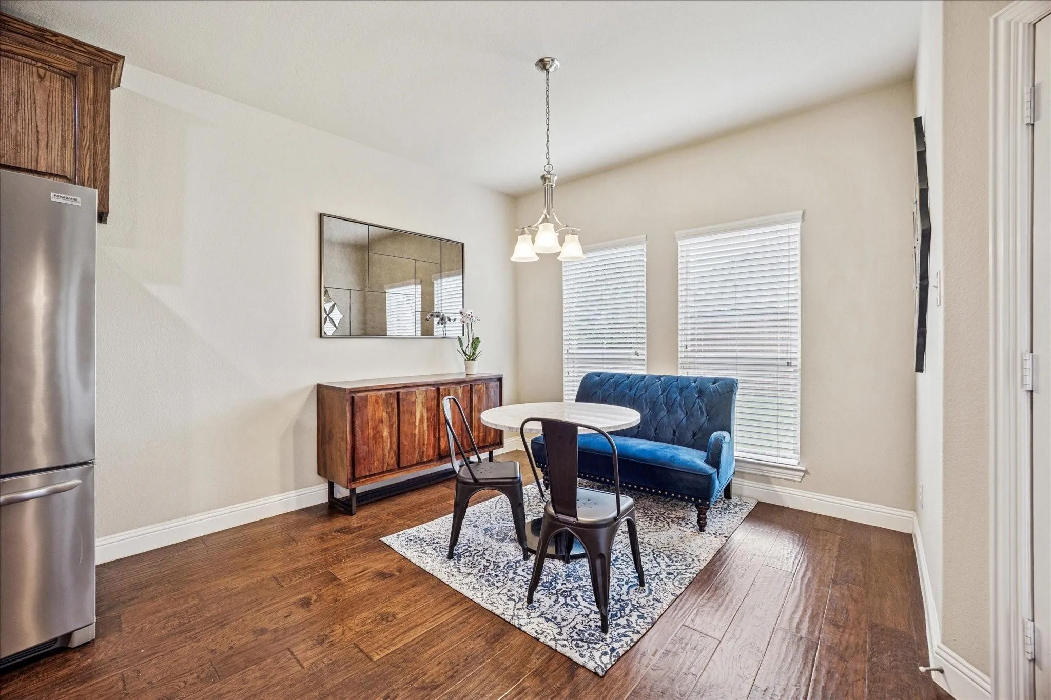 Hardwood-finish flooring, two windows with blinds, a built-in wood cabinet, and a stainless steel refrigerator