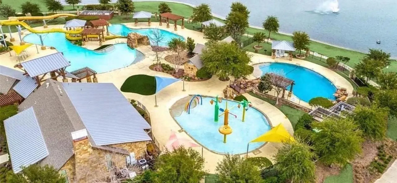 Expansive aquatic facility featuring multiple swimming pools, water slides, a splash pad, and shaded lounge areas, all situated adjacent to a body of water