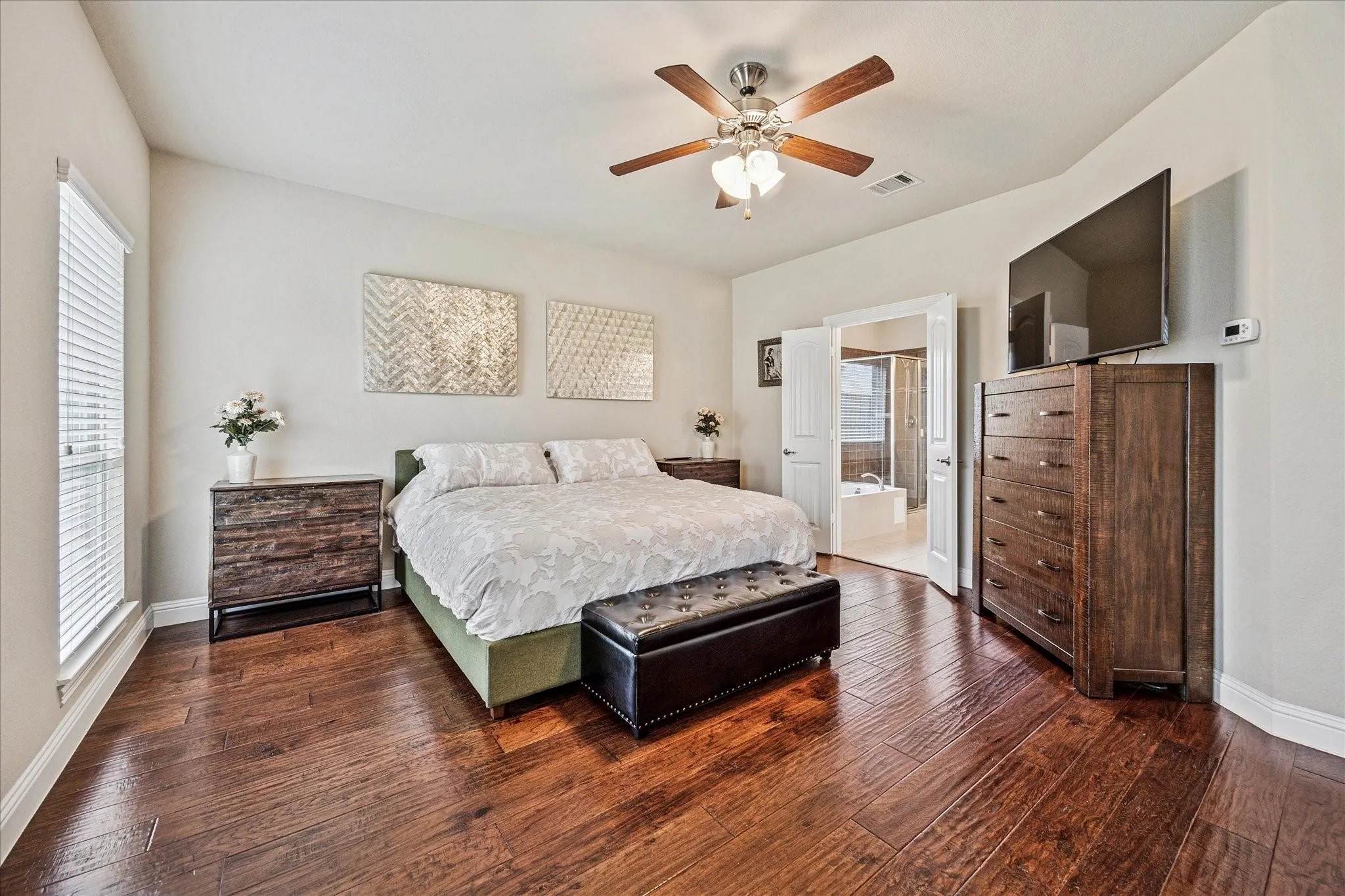 Hardwood-style flooring, window with blinds, ceiling fan with integrated lighting, double doors, and a built-in bathtub in the background