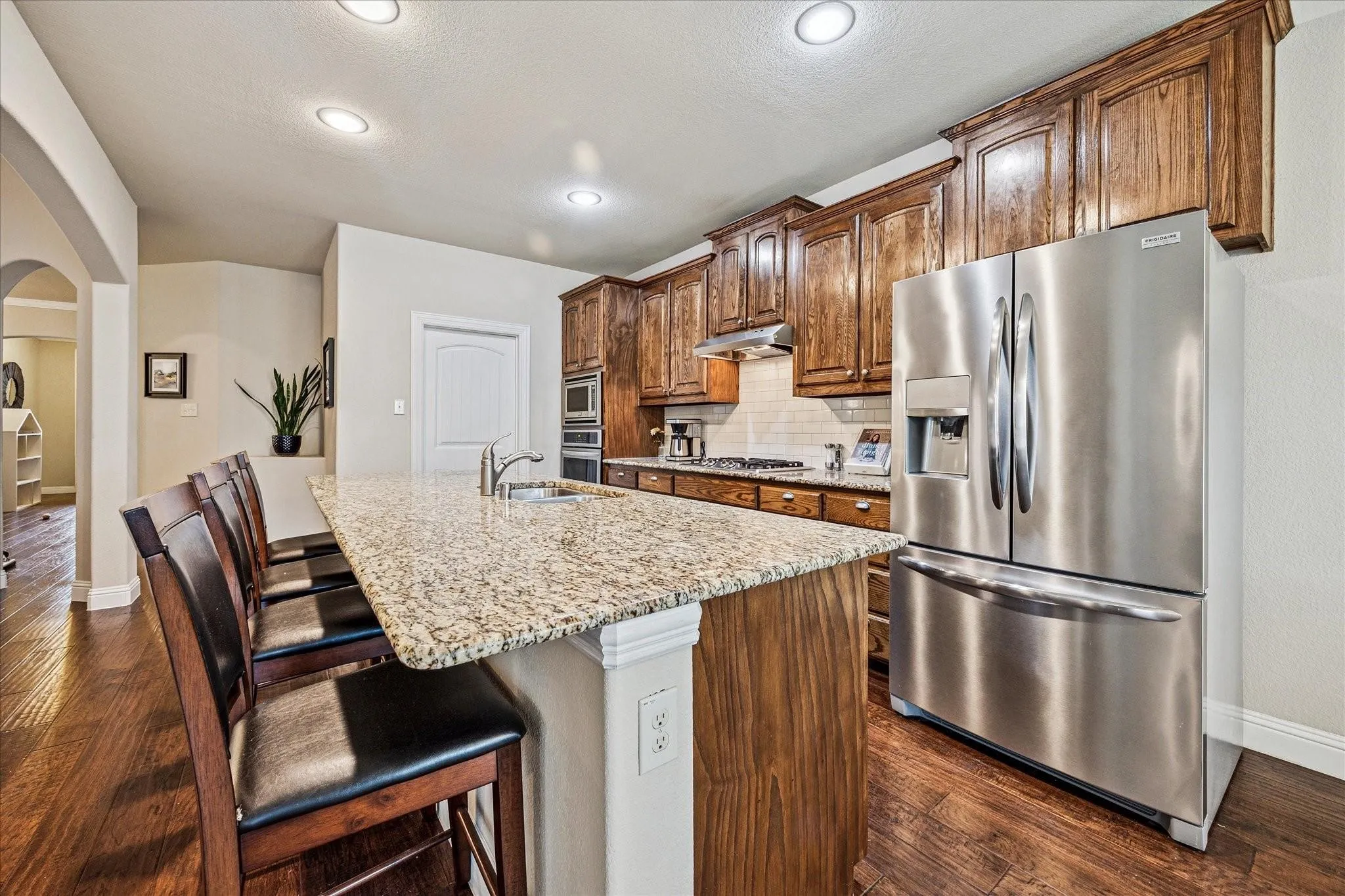 Kitchen featuring wood-finish flooring, recessed lighting, a stone countertop island, wood cabinetry, and stainless steel appliances