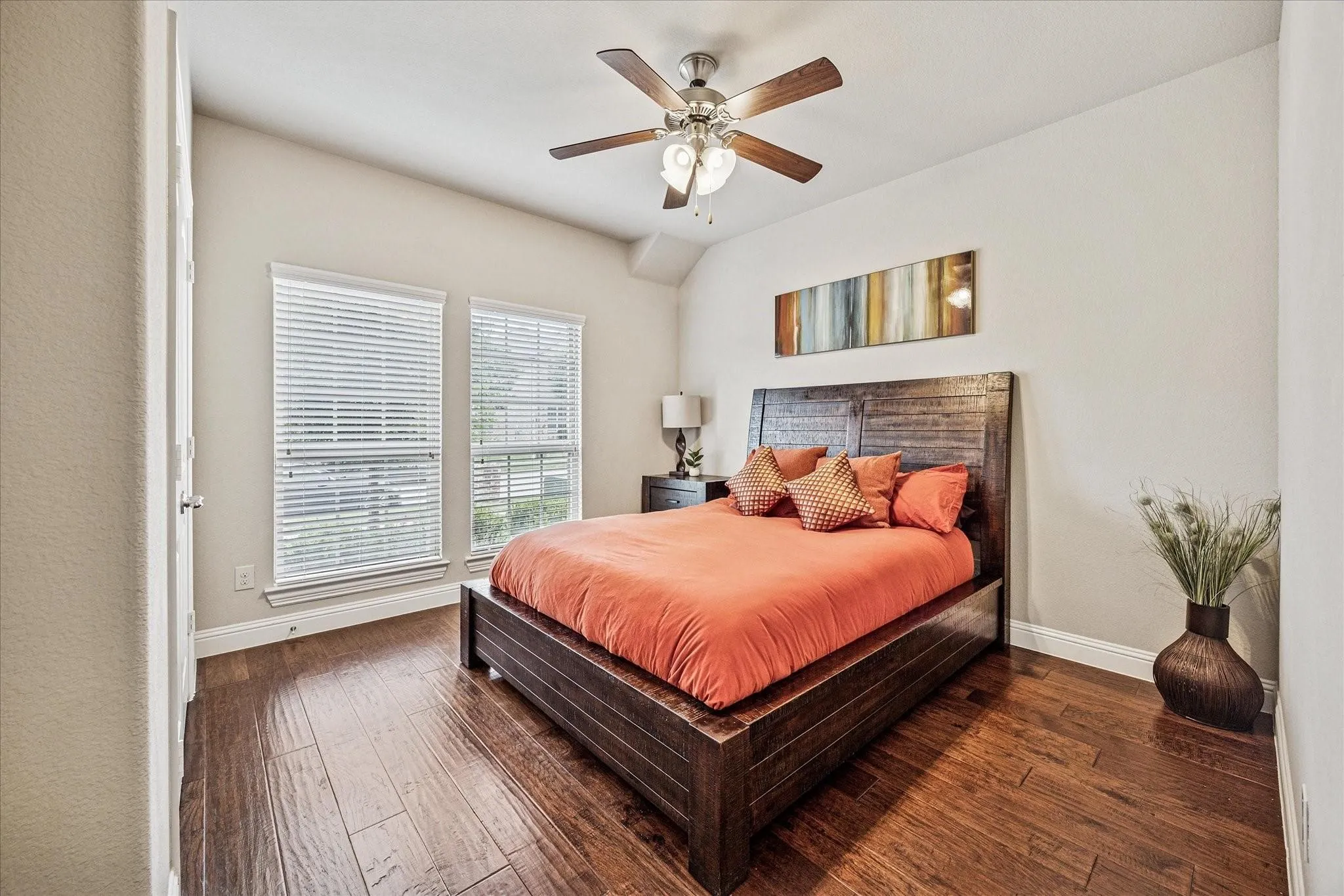 Vaulted ceiling with a ceiling fan, dual windows with blinds, wood-finish flooring, and light-toned walls