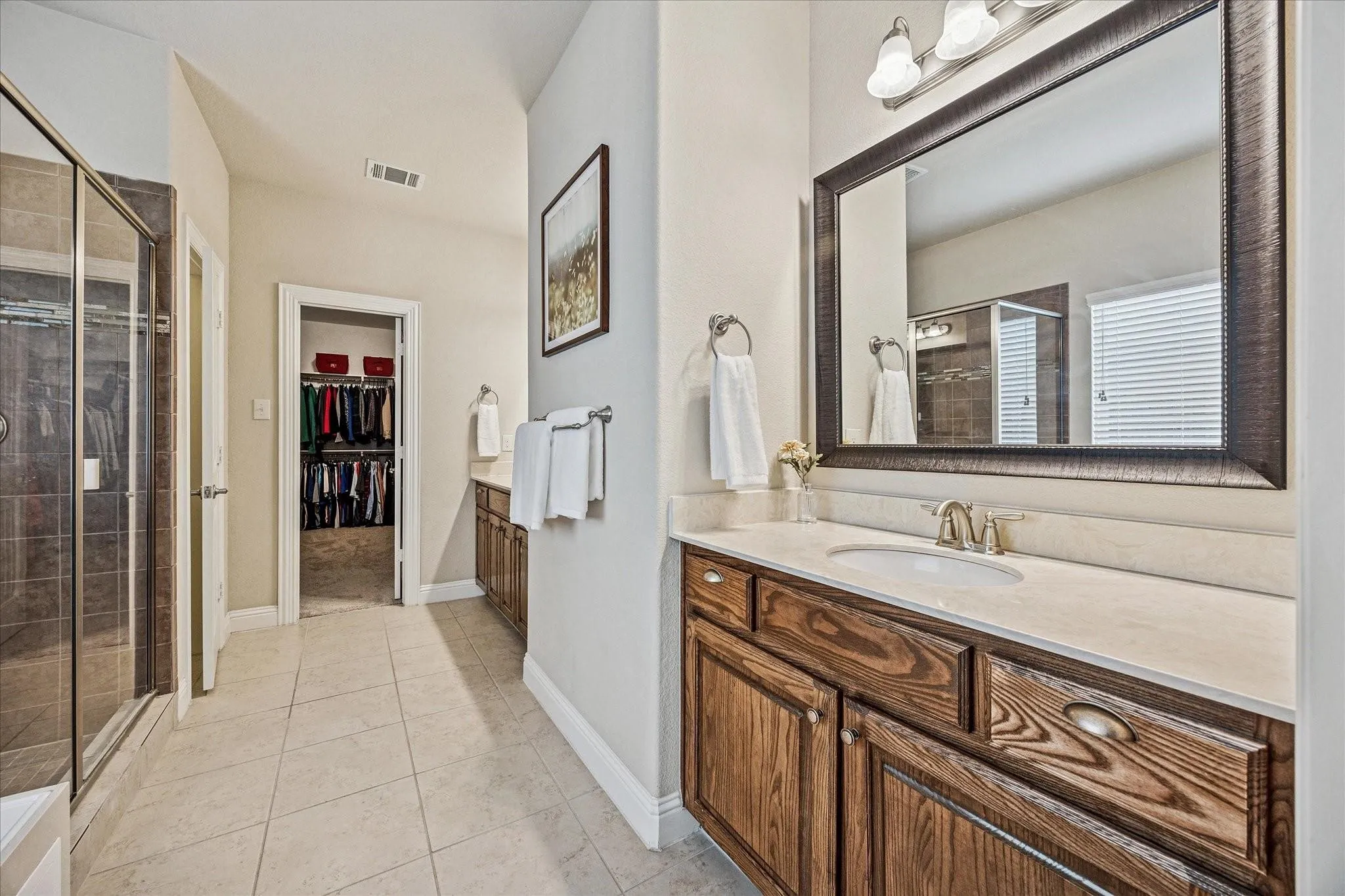 Dual wood-finish vanities with undermount sinks, a framed mirror, a glass-enclosed shower, and tile flooring
