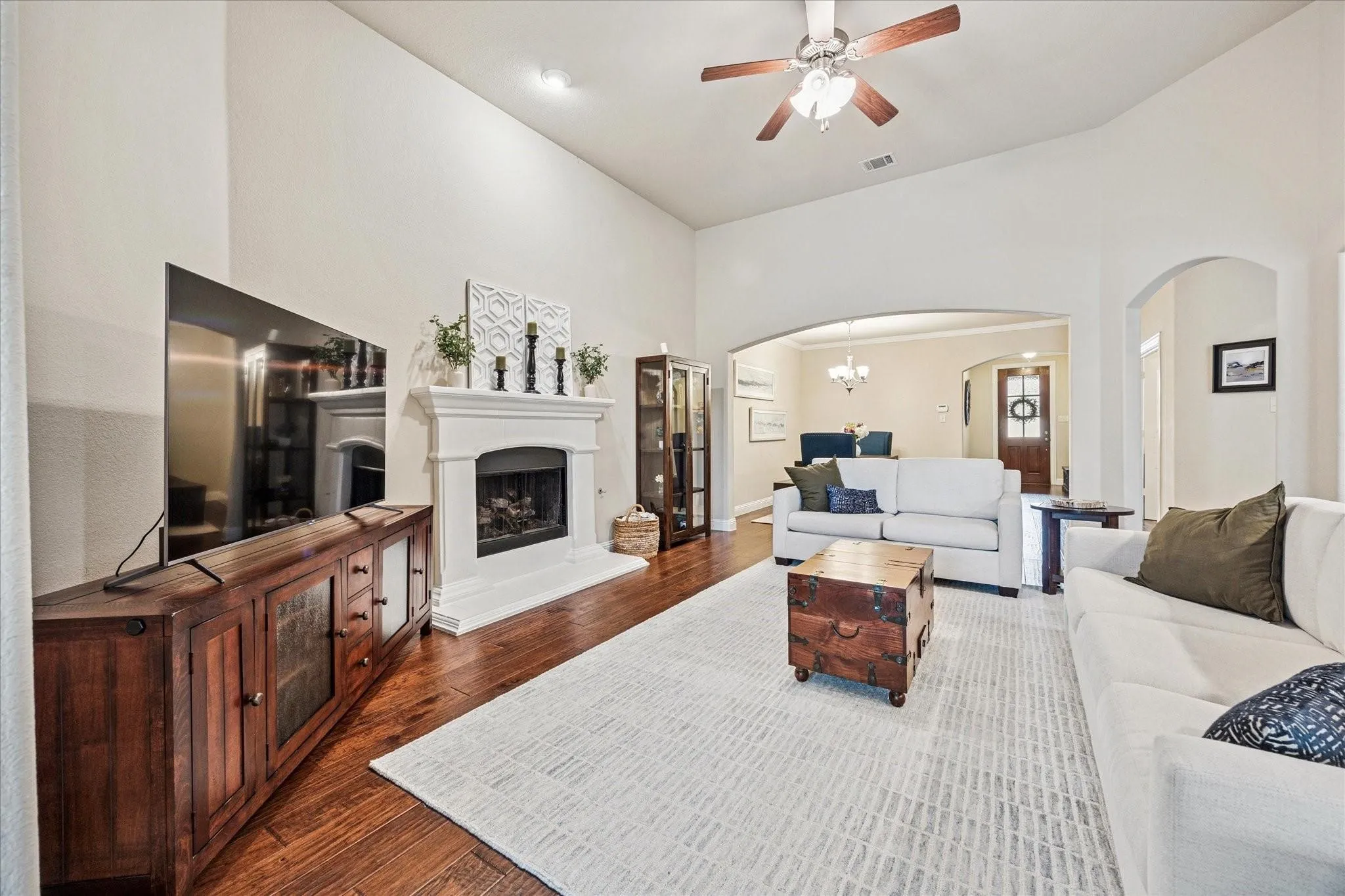 Vaulted ceiling, wood-finish flooring, white mantel fireplace, ceiling fan, and arched doorways