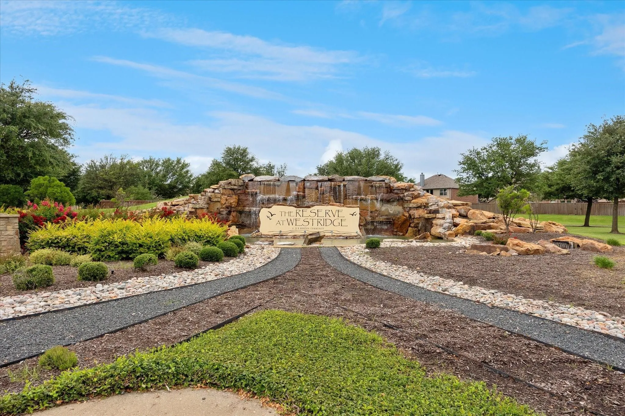 Stone entry monument featuring a cascading waterfall, stone landscaping, mature trees, and varied plantings