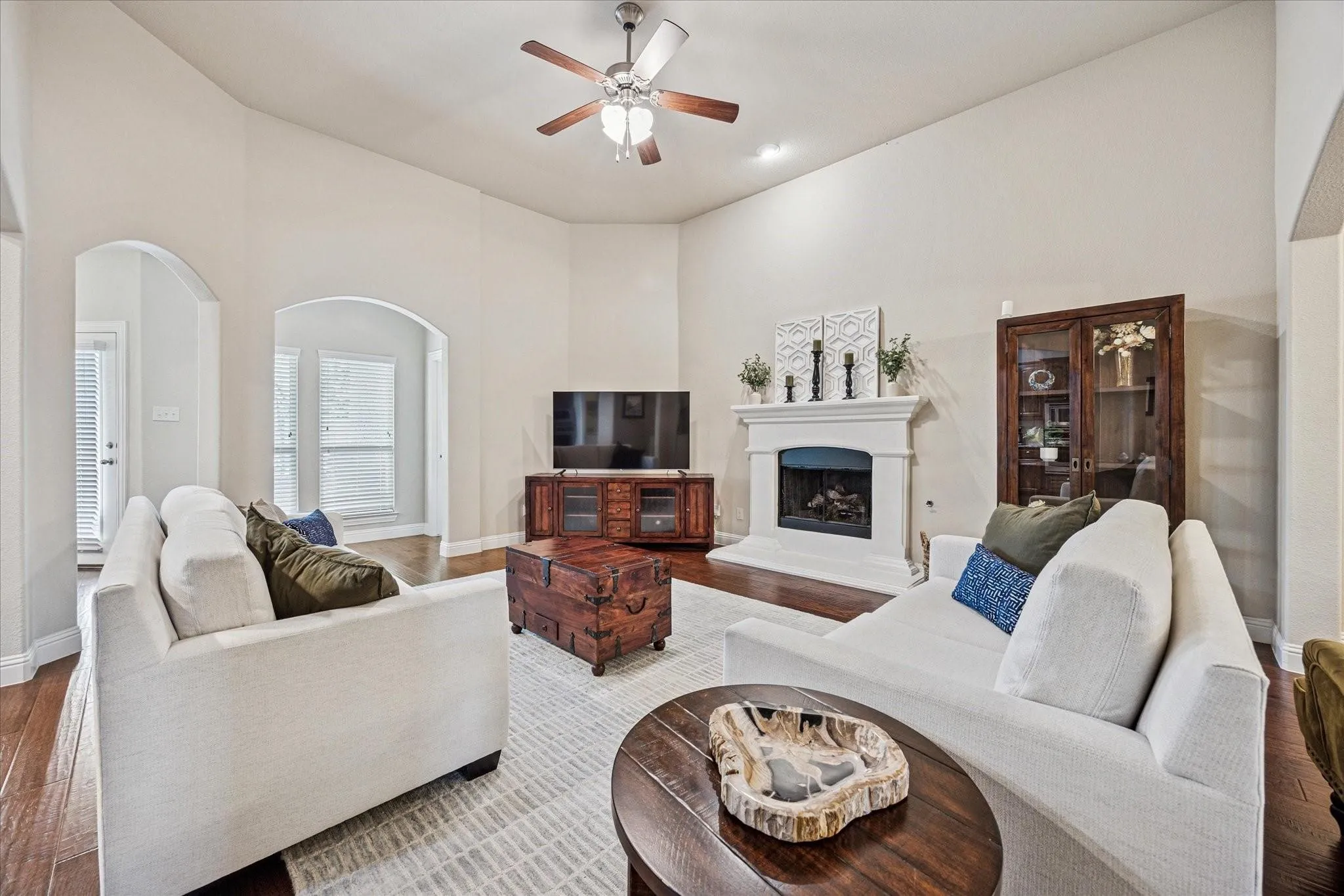 Vaulted ceiling with a ceiling fan, arched doorways, a built-in fireplace, and wood-finish flooring