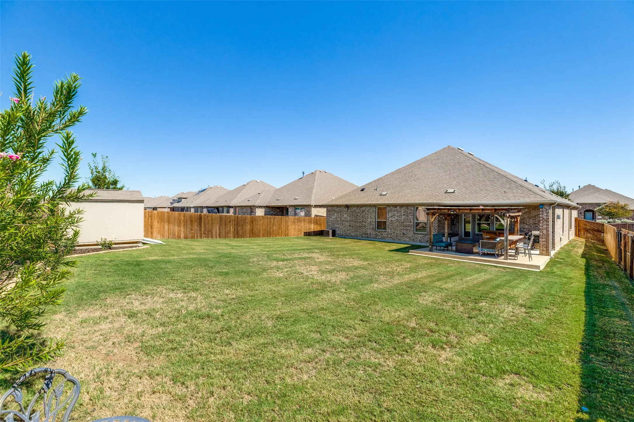 Expansive backyard with a manicured lawn, full wood fencing, and a concrete patio featuring a pergola