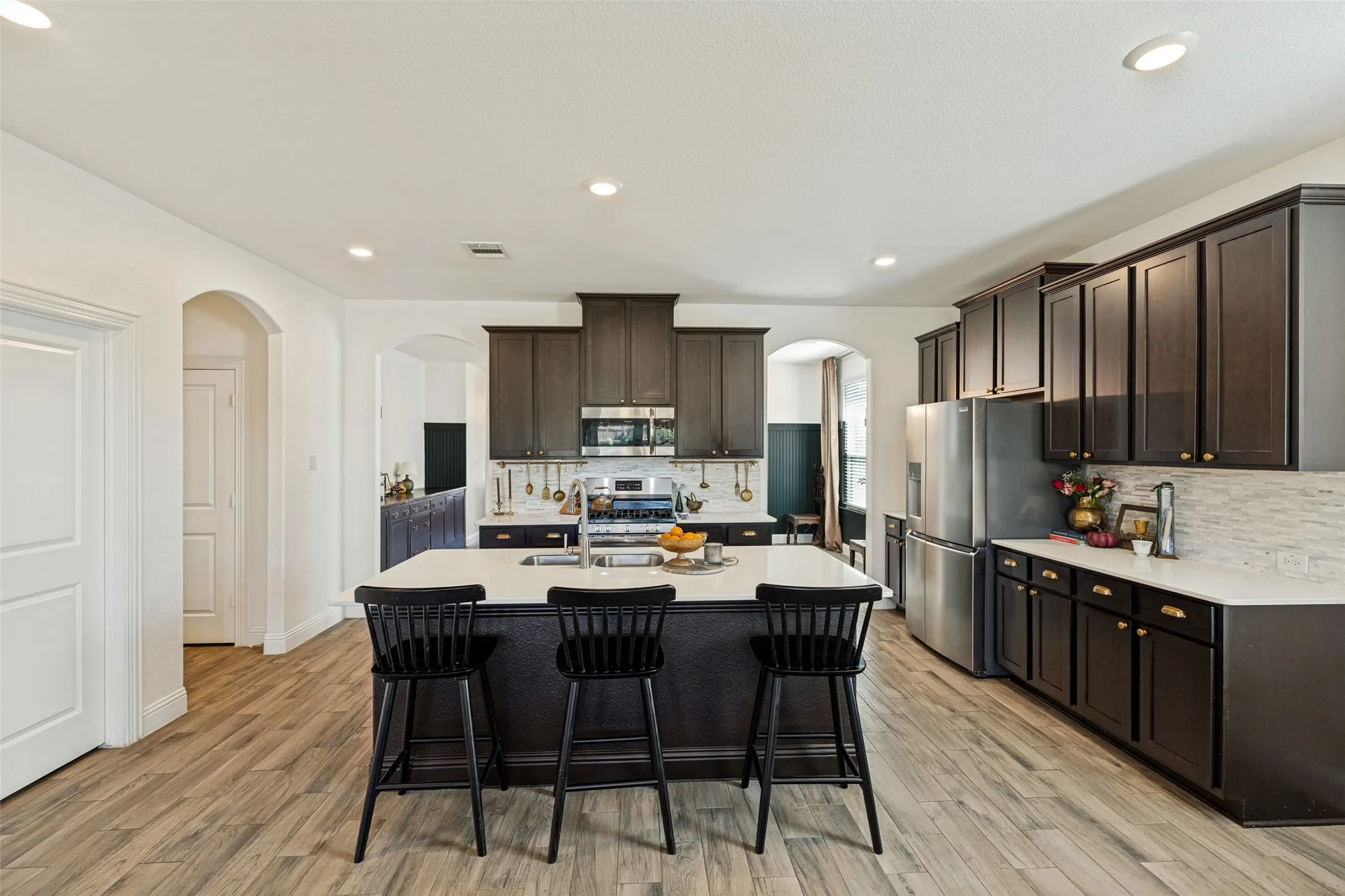Kitchen featuring wood-finish flooring, dark wood cabinetry, stainless steel appliances, a center island with a light-colored countertop, and recessed lighting