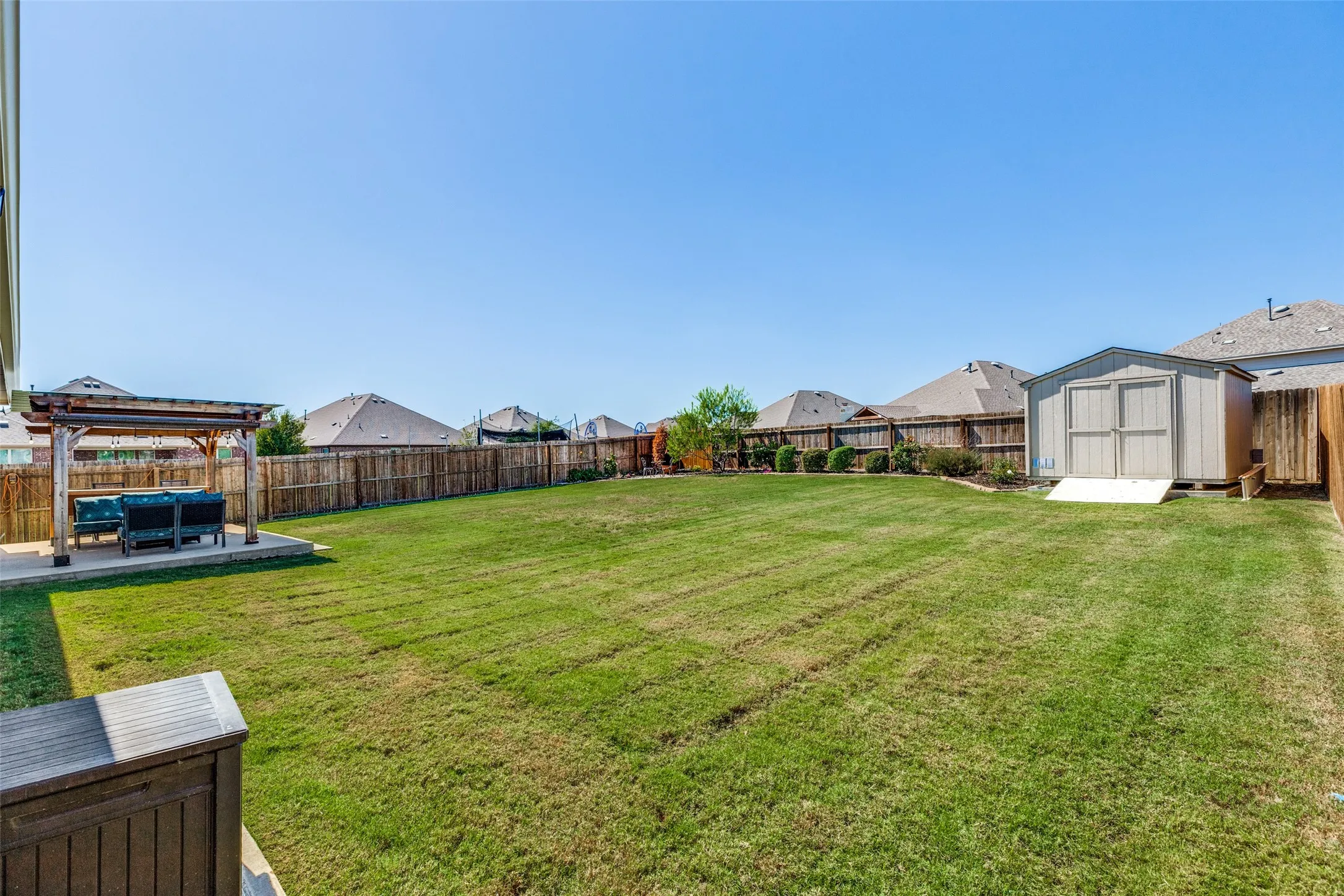 Expansive backyard with a large grassy area, a wooden privacy fence, a detached shed, and a paved patio area