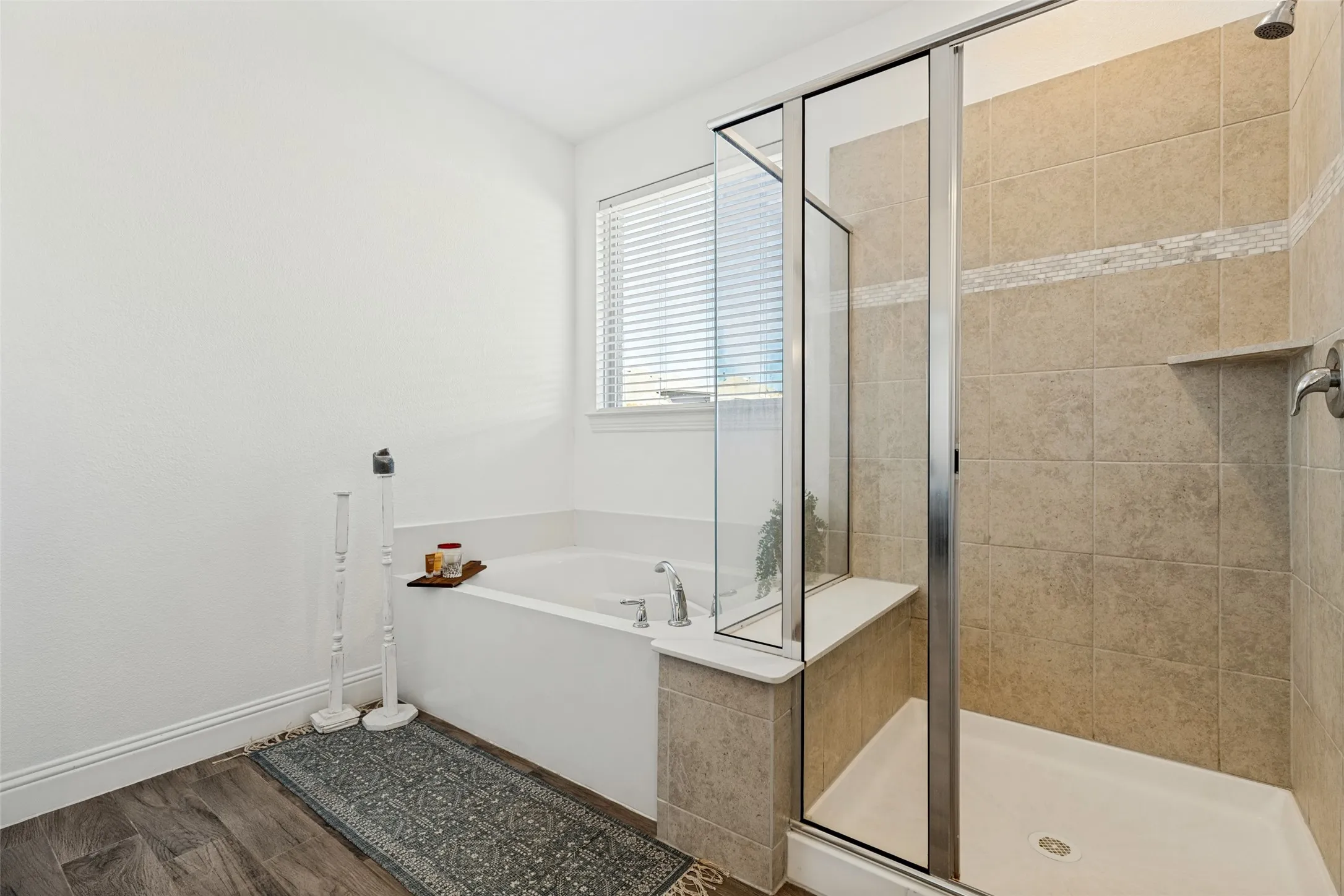 Soaking tub with a window, glass-enclosed shower, tile-surround shower, and wood-finish flooring