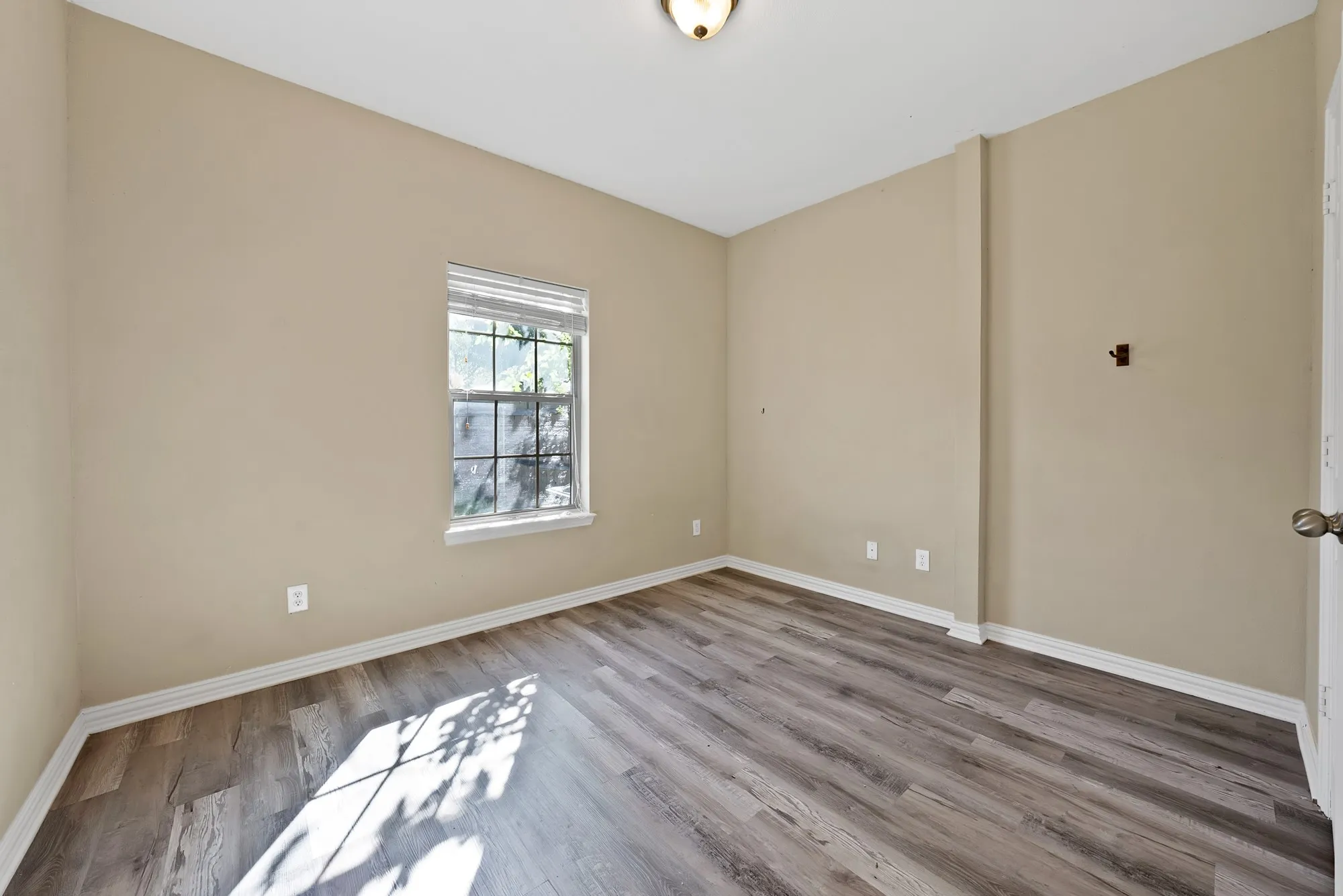 downstairs primary bedroom. Wood-look flooring, ceiling light, and a window with natural light. Separate full bath located nearby on the main level.