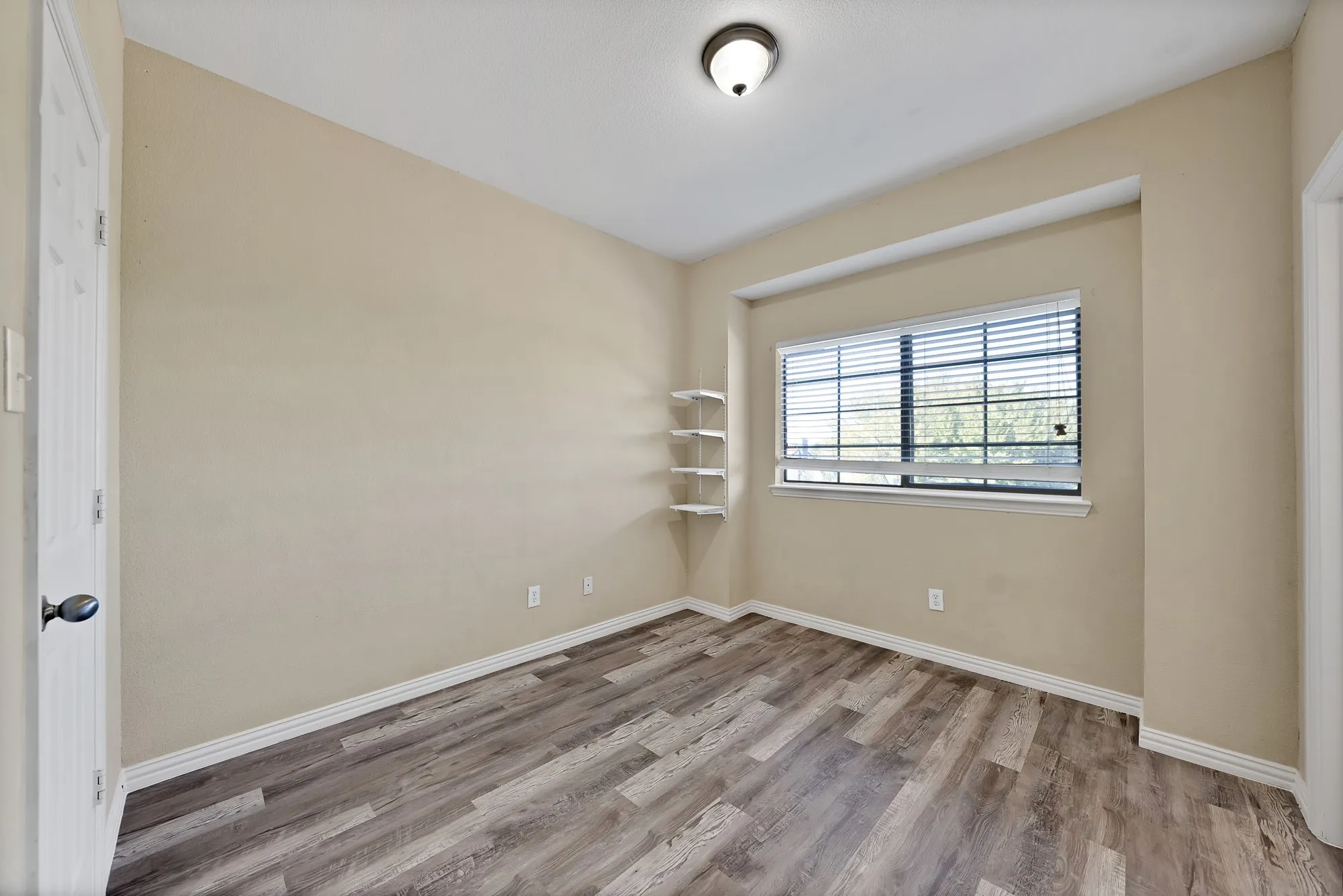 Bedroom: Large window with blinds, wood-look flooring, and ceiling light.