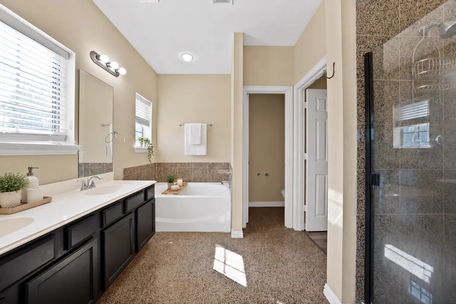 Upstairs primary bathroom Upstairs primary ensuite bath: Dual-sink vanity with dark cabinetry, garden tub with tile surround, and separate walk-in shower with glass door and floor-to-ceiling tile. Private water closet and tile flooring.