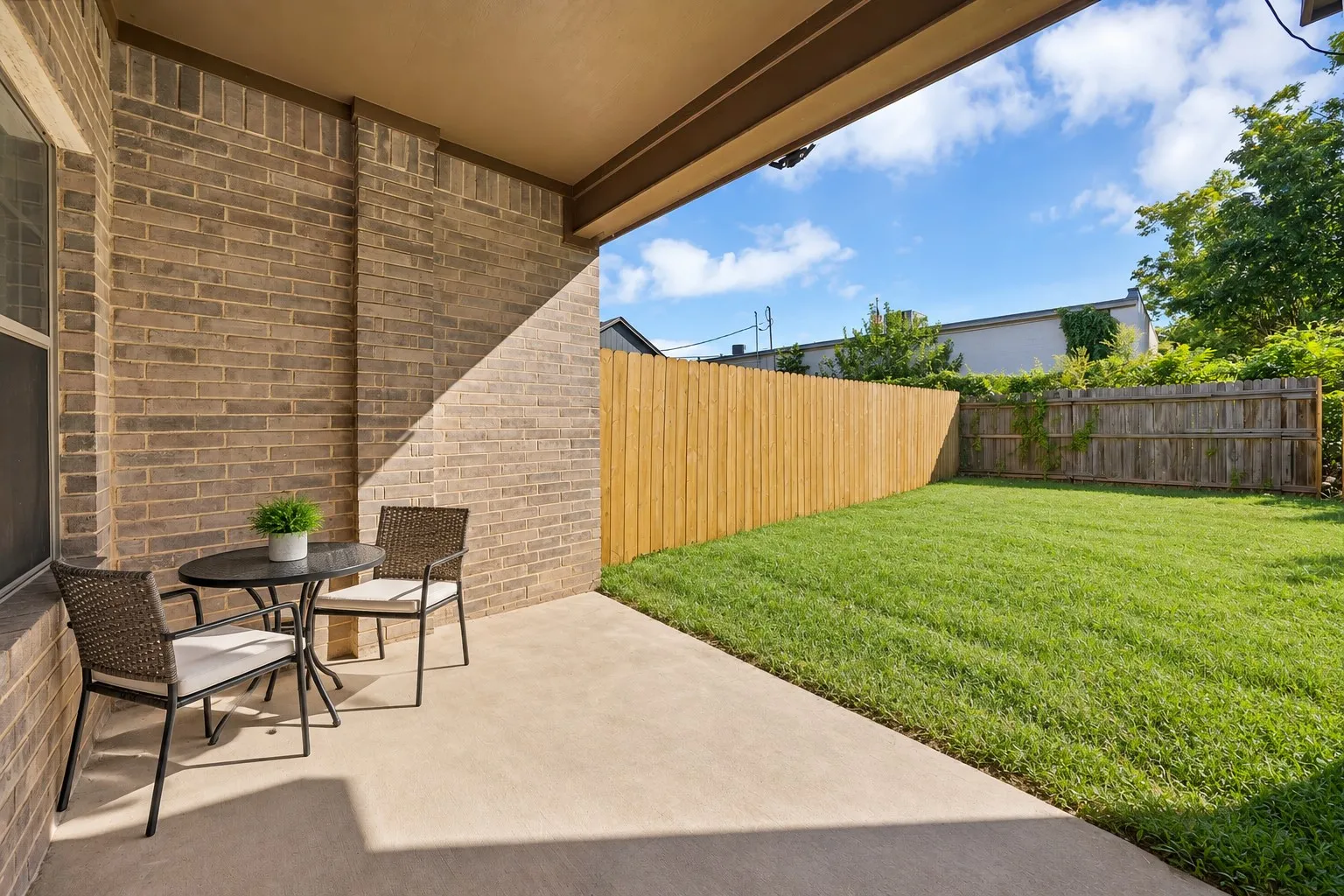 Backyard: Covered concrete patio with brick exterior and grass yard. Wood privacy fencing with new cedar fence panels along one side.