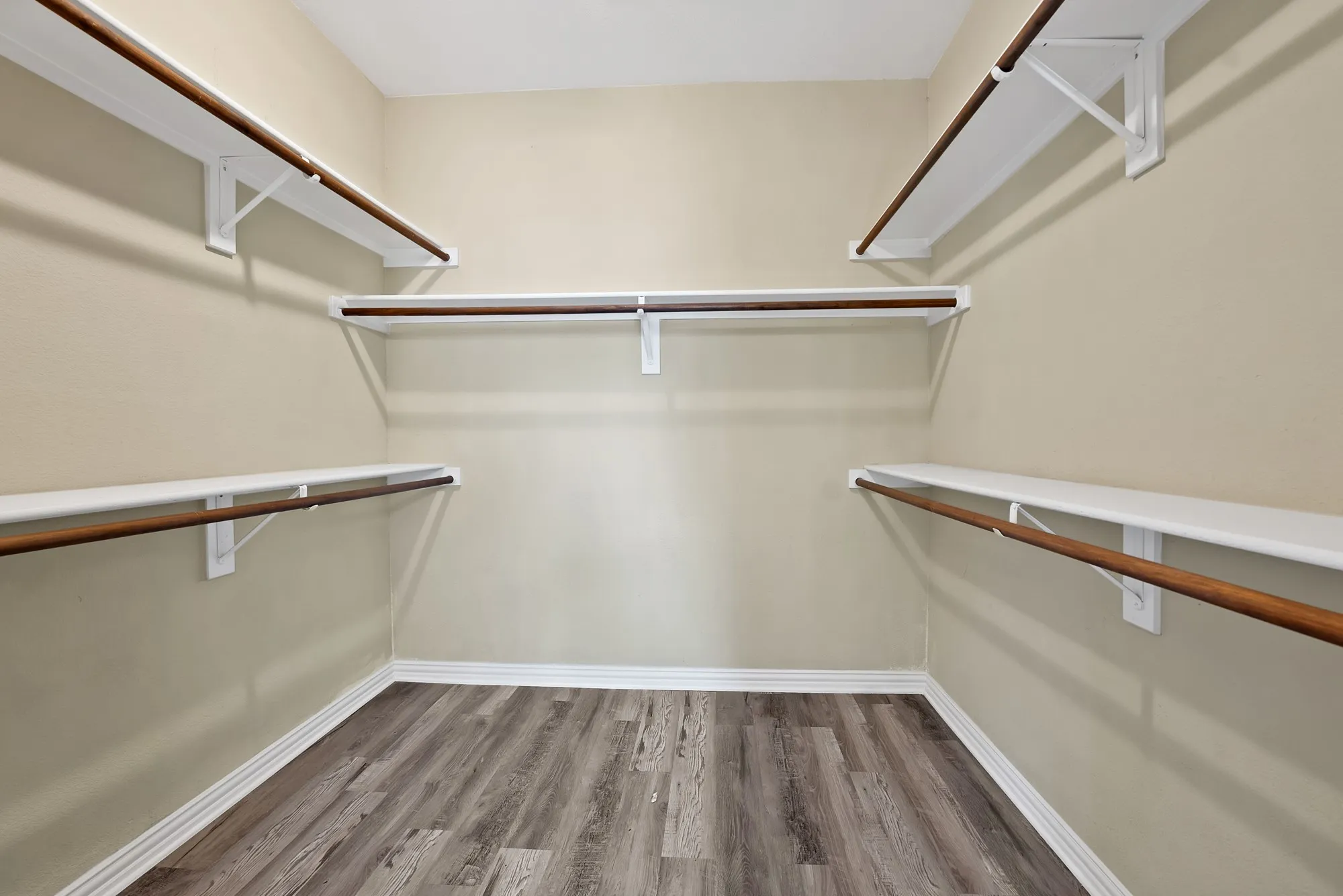 Primary Closet Walk-in closet: Double hanging rods and shelving on three walls with wood-look flooring.