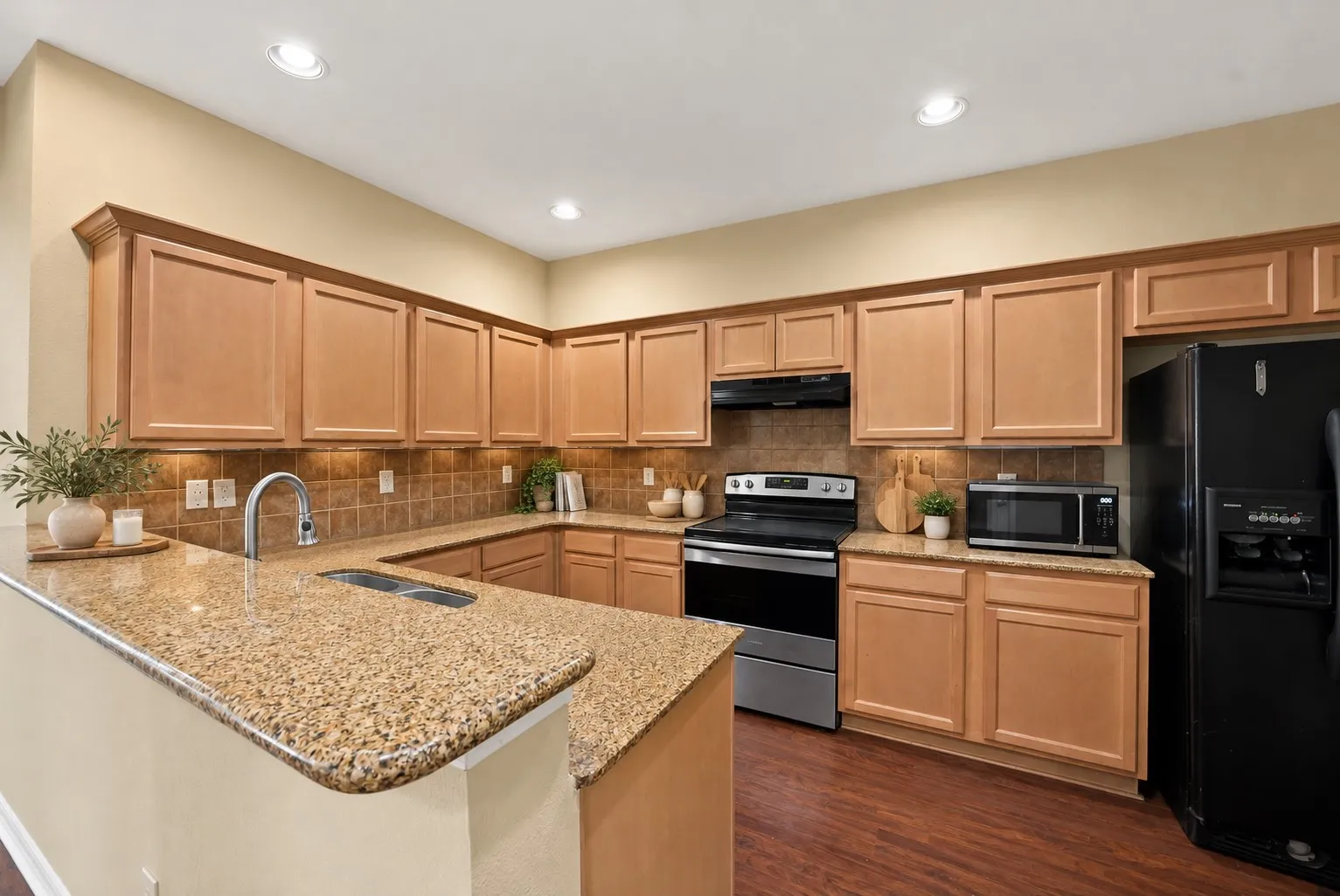 Kitchen: Granite countertops, tile backsplash, and maple-tone cabinetry with crown molding. Stainless steel electric range, recessed lighting, and double-basin sink on the peninsula.