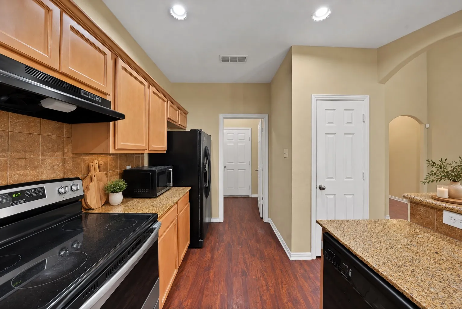 Kitchen and hallway: Granite countertops, stainless electric range, and black side-by-side refrigerator. Hallway leads to additional rooms and storage.