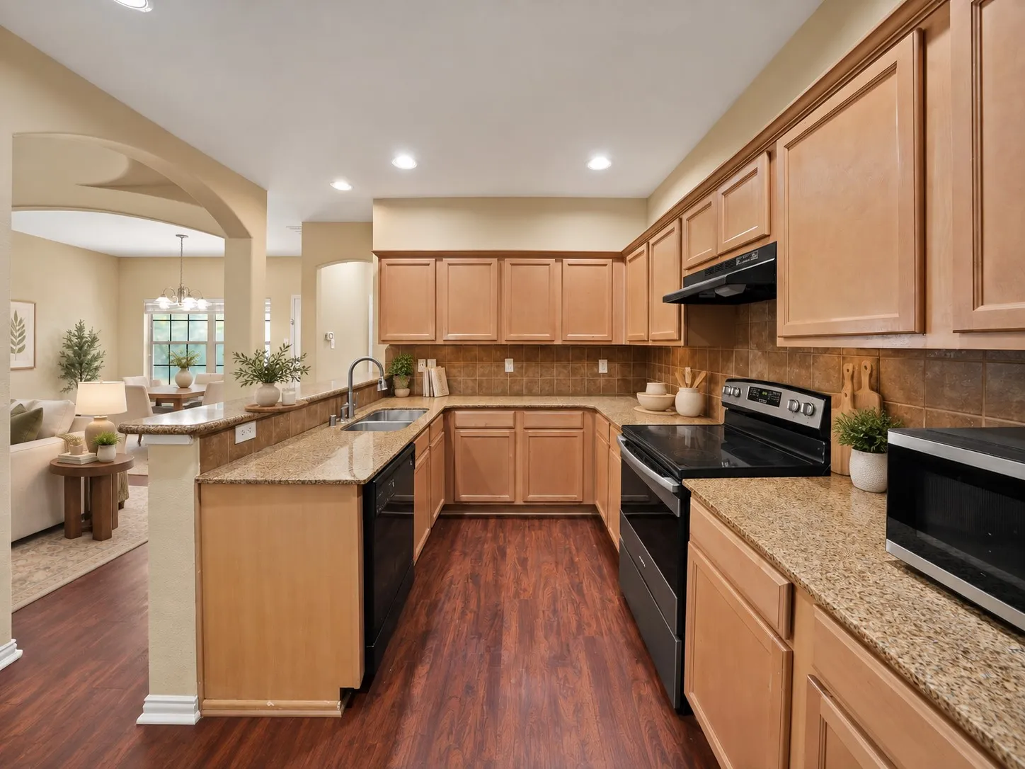 Kitchen: U-shaped layout with granite countertops and raised breakfast bar open to the living room. Black dishwasher, stainless electric range, and under-cabinet range hood.