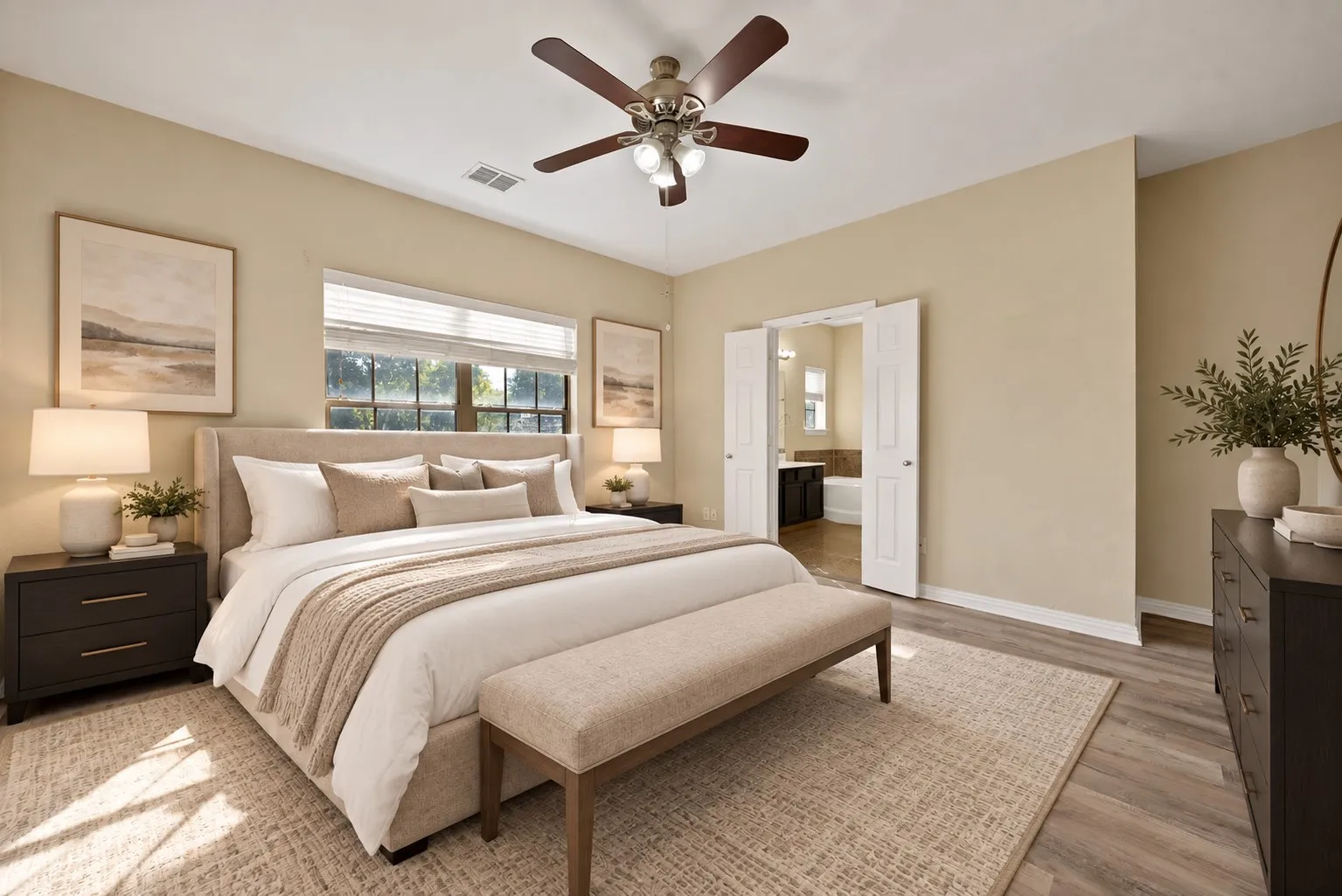 Upstairs primary bedroom with ensuite bathroom - virtually staged Wood-look flooring, ceiling fan with light kit, and a wide window with blinds. Double doors open to the ensuite bath with garden tub.