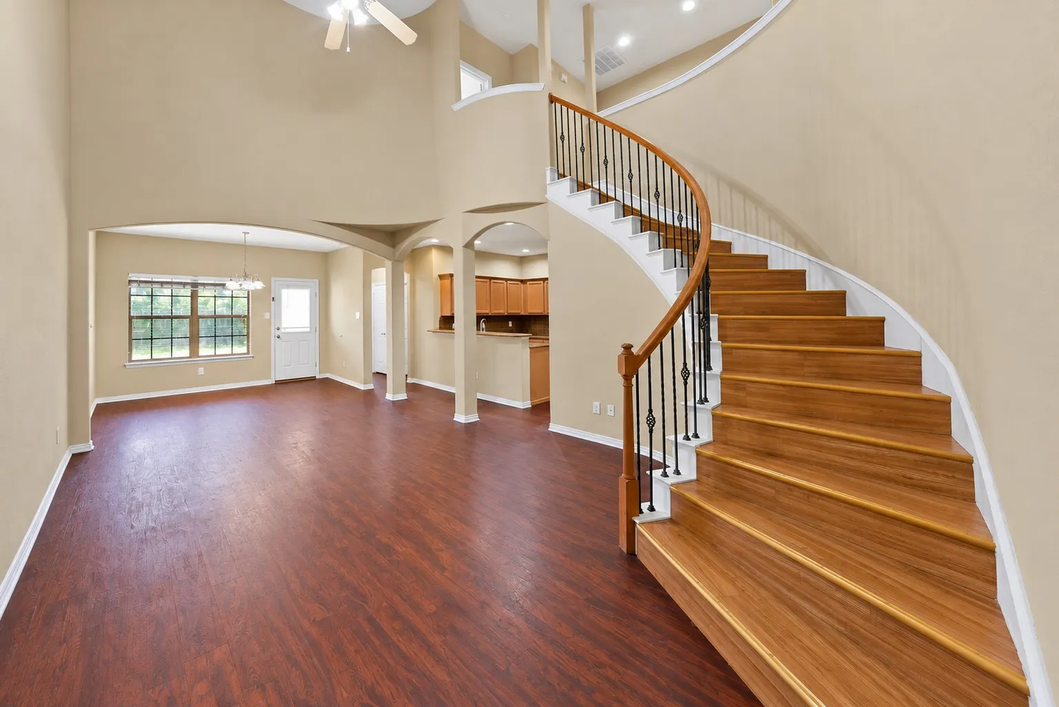 Living room: Two-story ceiling with ceiling fan and a curved staircase with wood handrail and wrought iron balusters. Open to the dining area and kitchen.