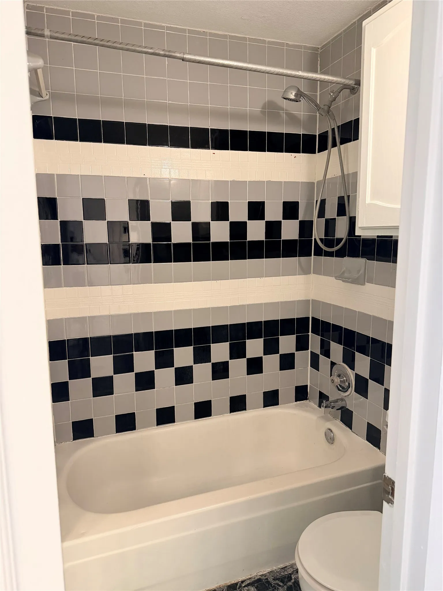 Bathtub and shower combination featuring a tiled surround in black, white, and gray