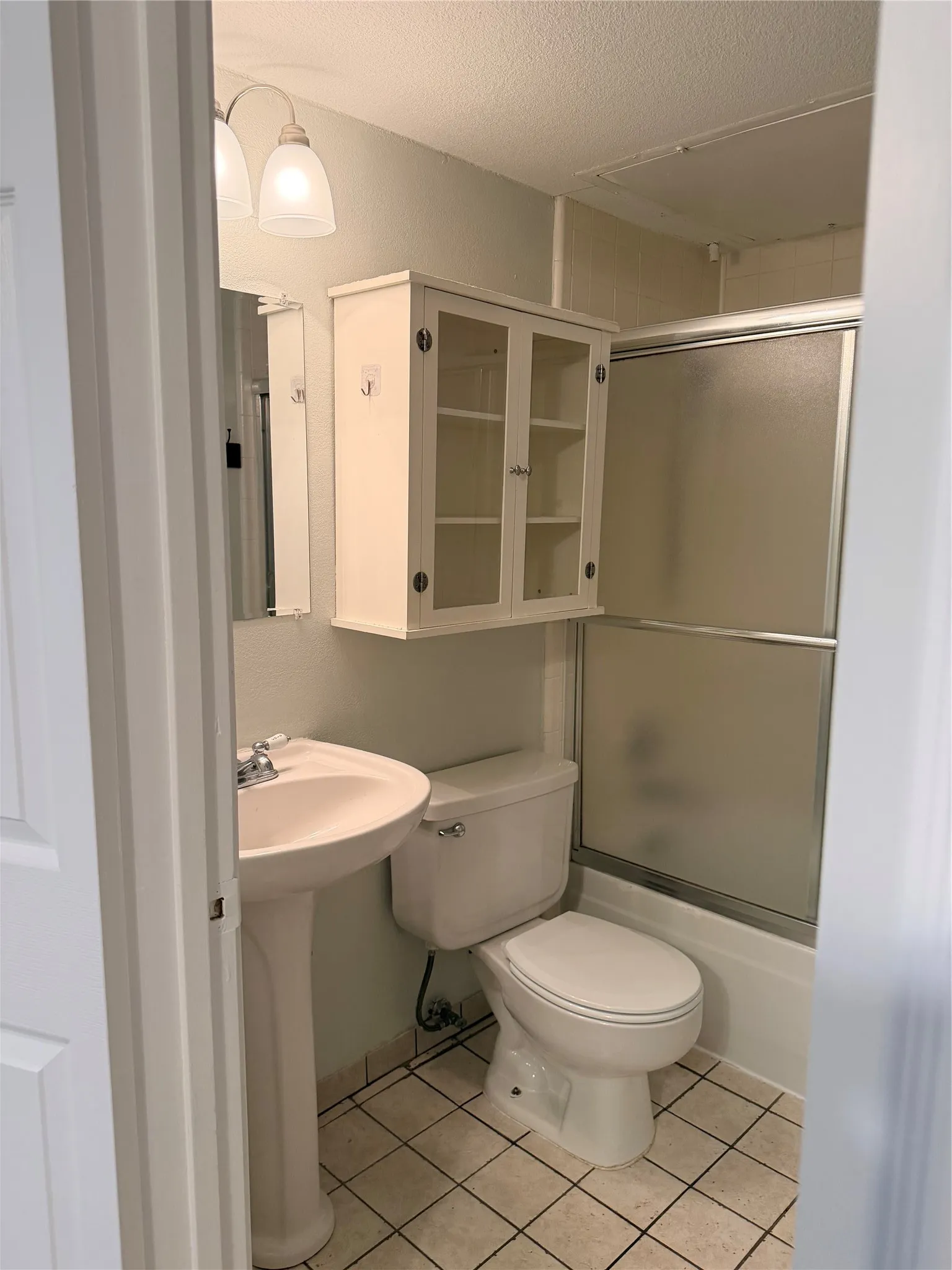 Pedestal sink with chrome faucet, wall-mounted storage cabinet, white toilet, and enclosed shower/tub combination