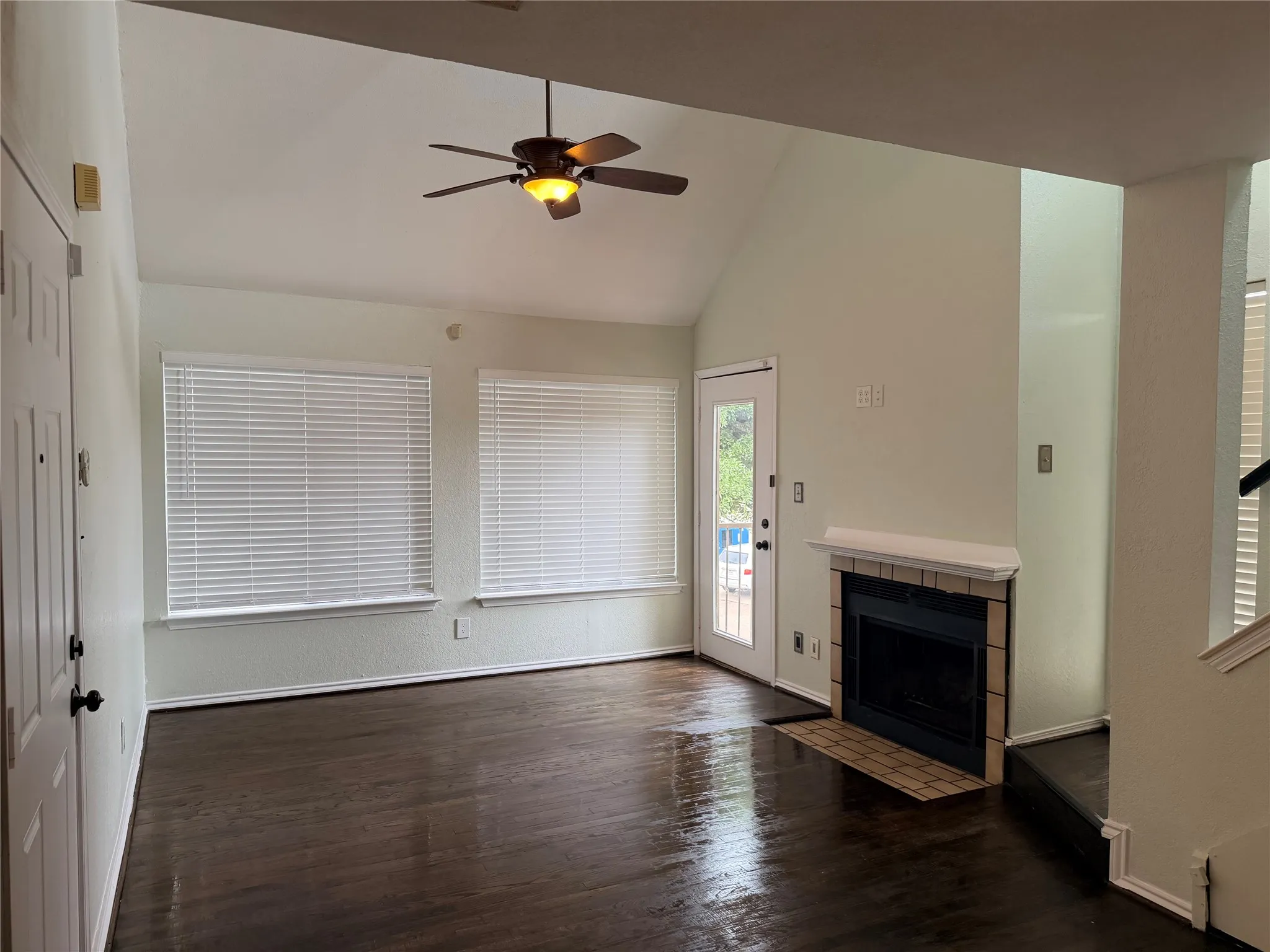 Vaulted ceiling with a ceiling fan, wood-finish flooring, and a fireplace with a brick​​‌​​​​‌​​‌‌​‌‌​​​‌‌​‌​‌​‌​​​‌​​ hearth