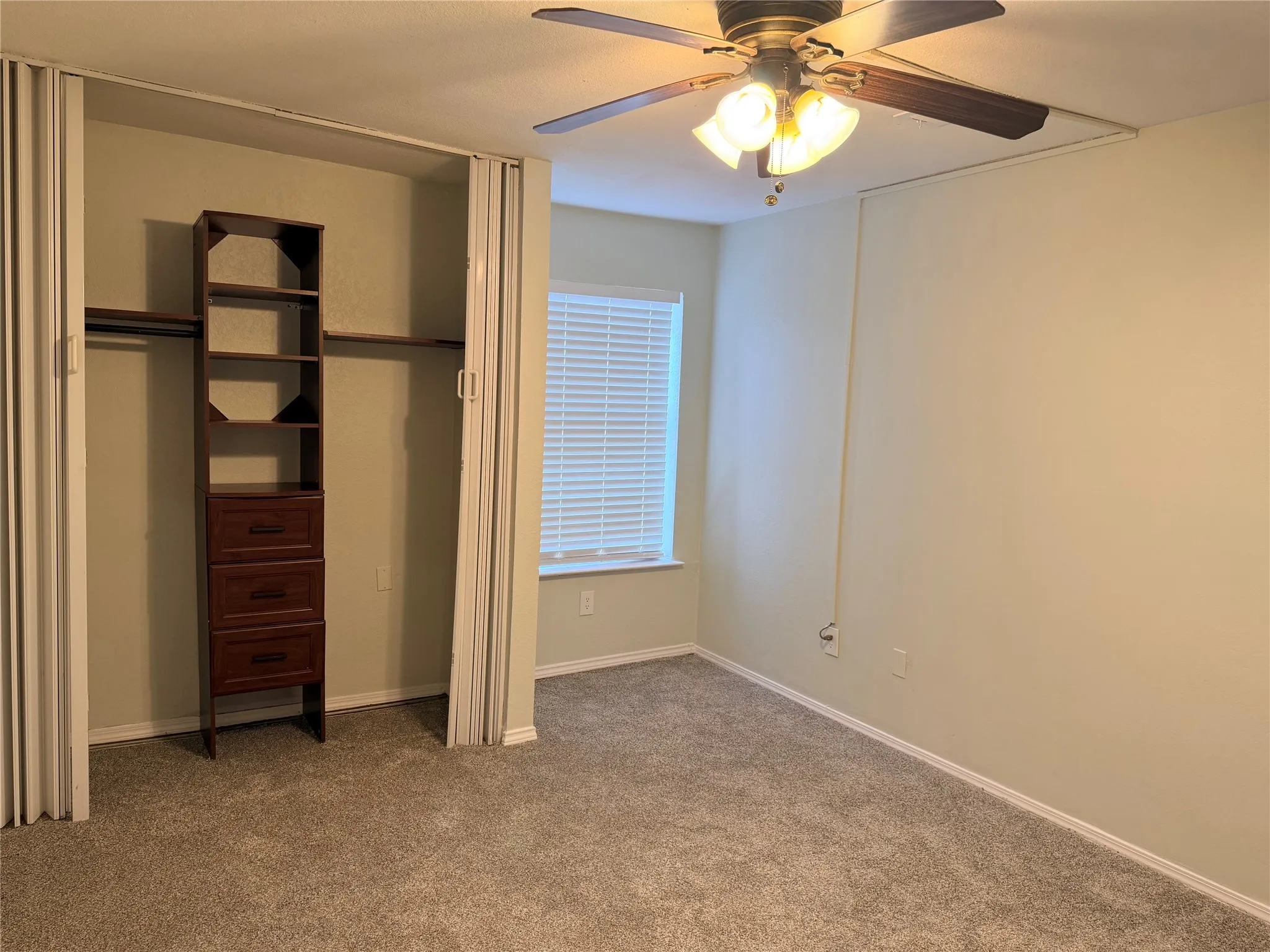 Integrated closet storage system, ceiling fan with light fixture, window with blinds, and neutral tone walls