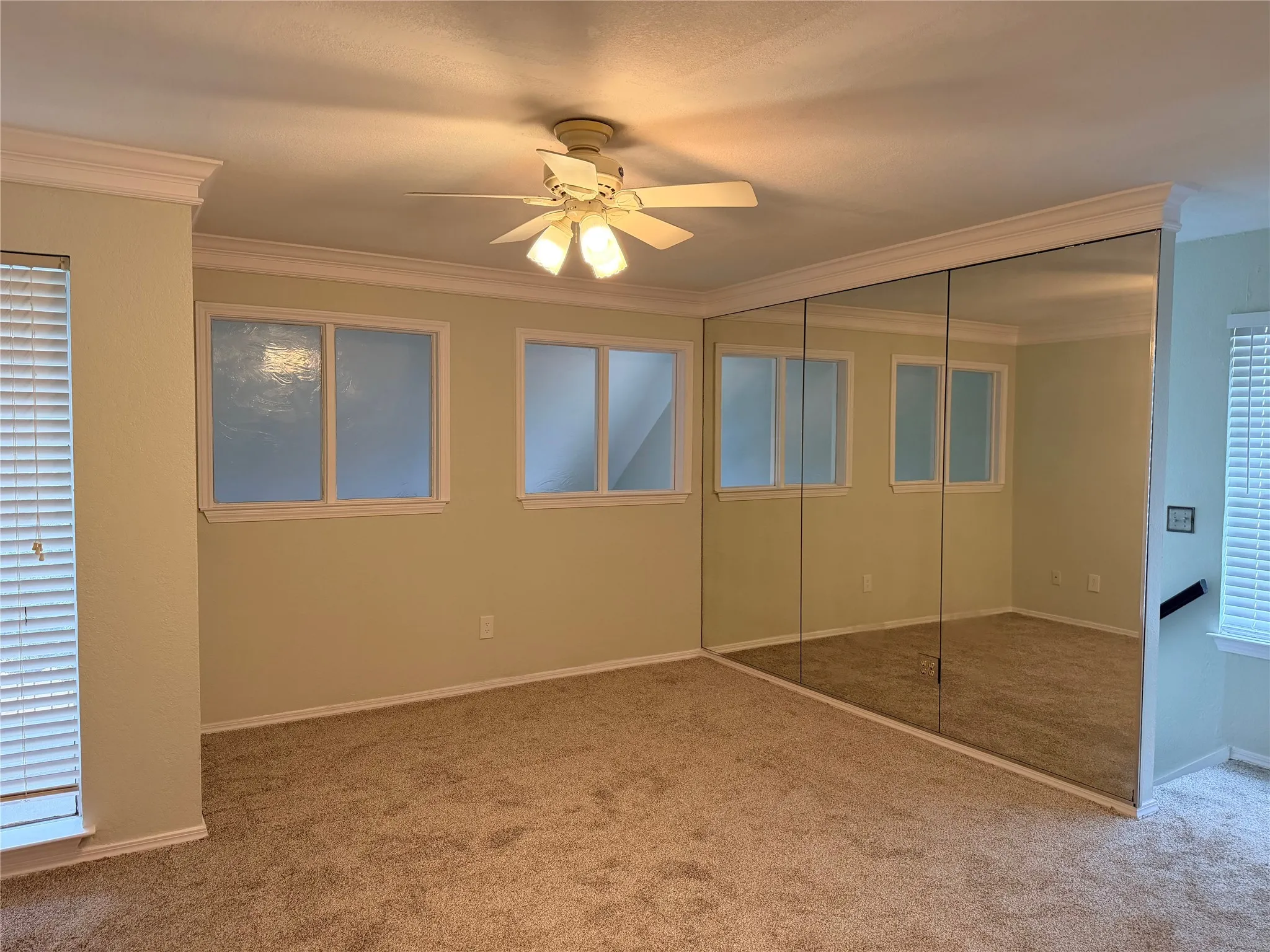 Primary Bedroom with Wall-to-wall mirror, ceiling fan with integrated lighting, multiple windows with blinds, and crown molding