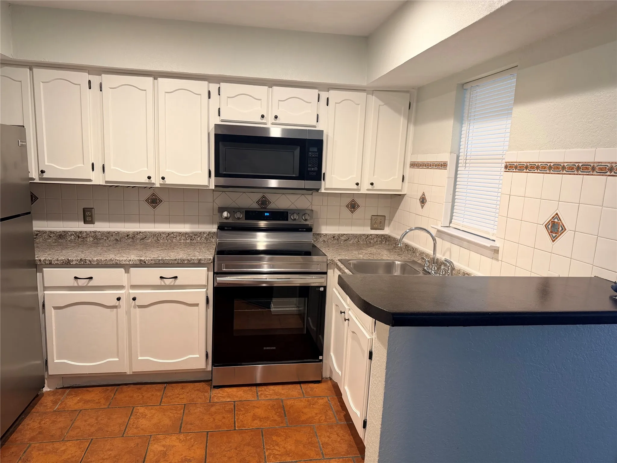 White cabinetry, stainless steel appliances, tile flooring, tile backsplash, and a breakfast bar