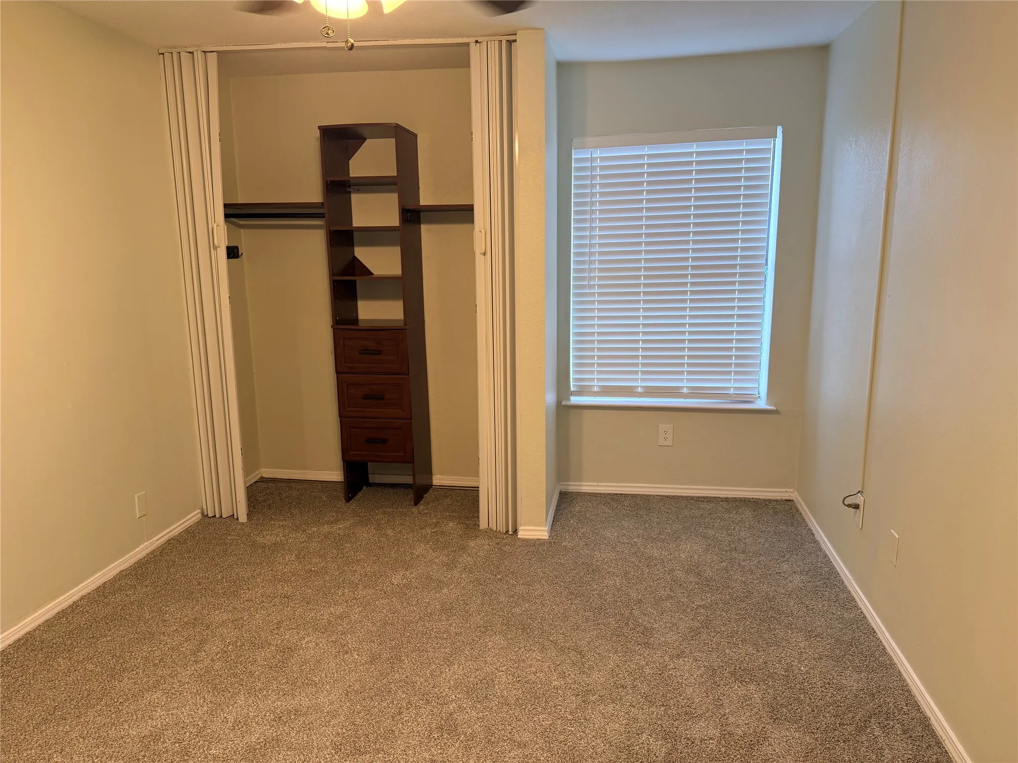 Secondary bedroom with Recessed closet with integrated shelving and drawers, accompanied by a window with blinds