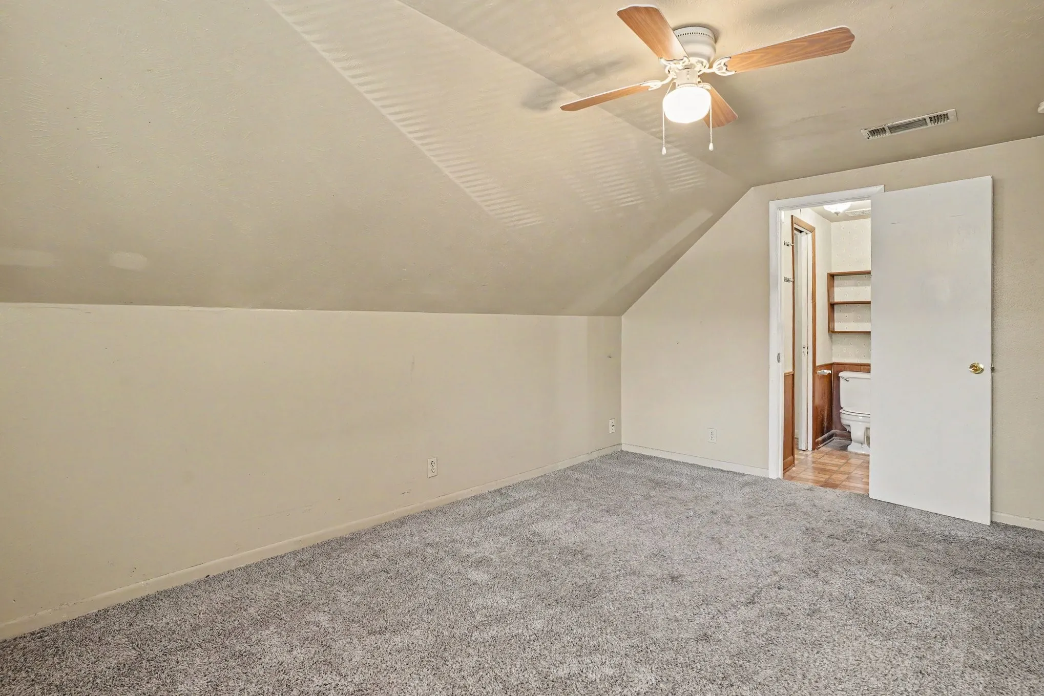 Sloped ceilings with a ceiling fan light fixture, carpeted flooring, and an adjoining room with built-in shelving