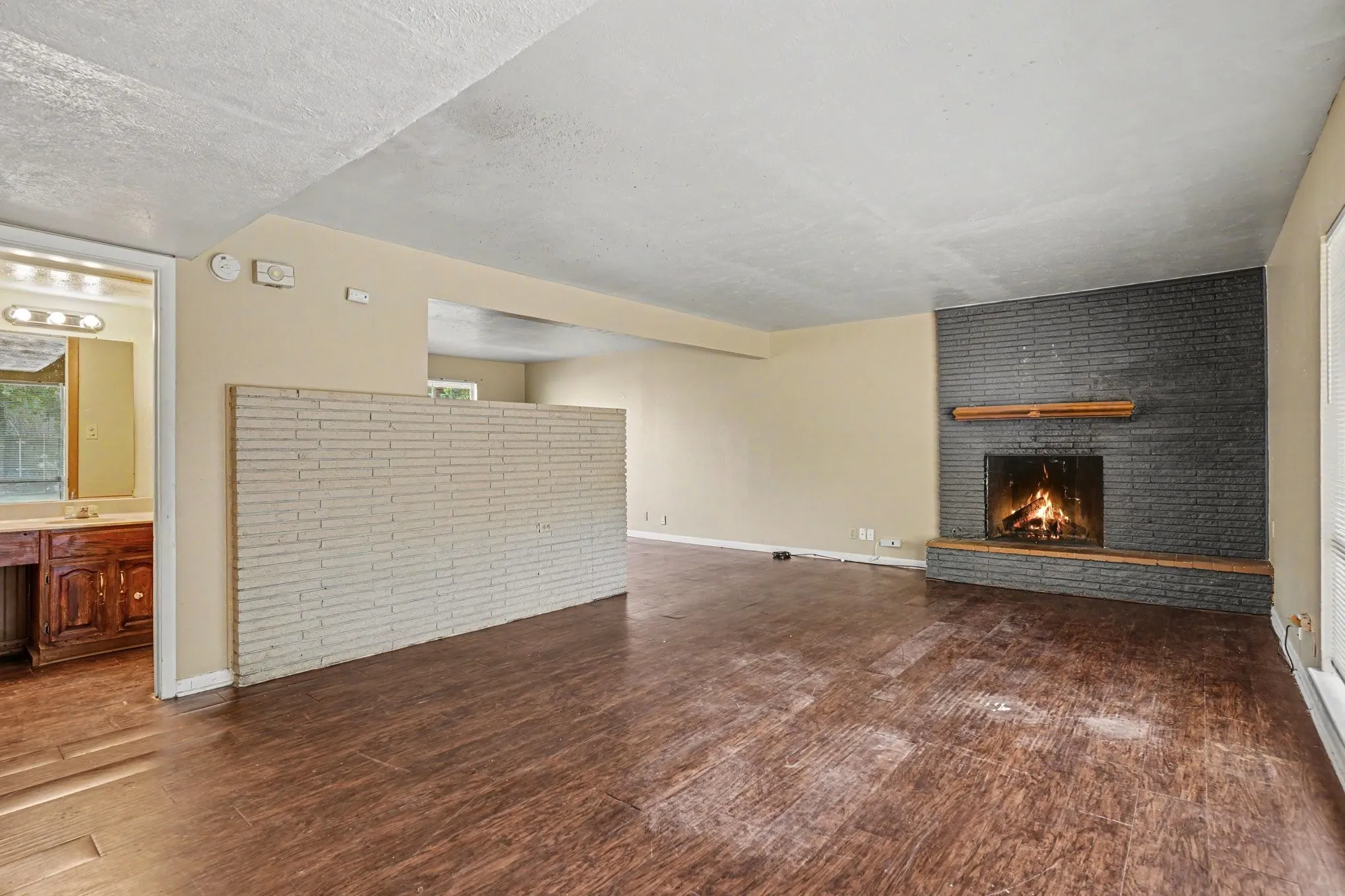 Spacious living area featuring a dark brick fireplace with a wood mantle, wood-finish flooring, and a half-wall partition