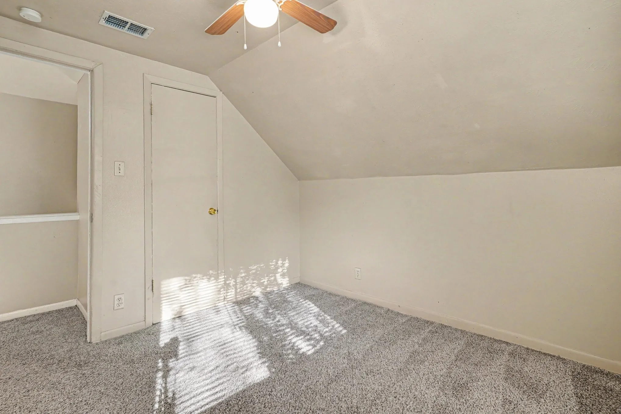 Sloped ceiling room featuring a ceiling fan with light, gray carpeting, and a closet with a gold-tone doorknob