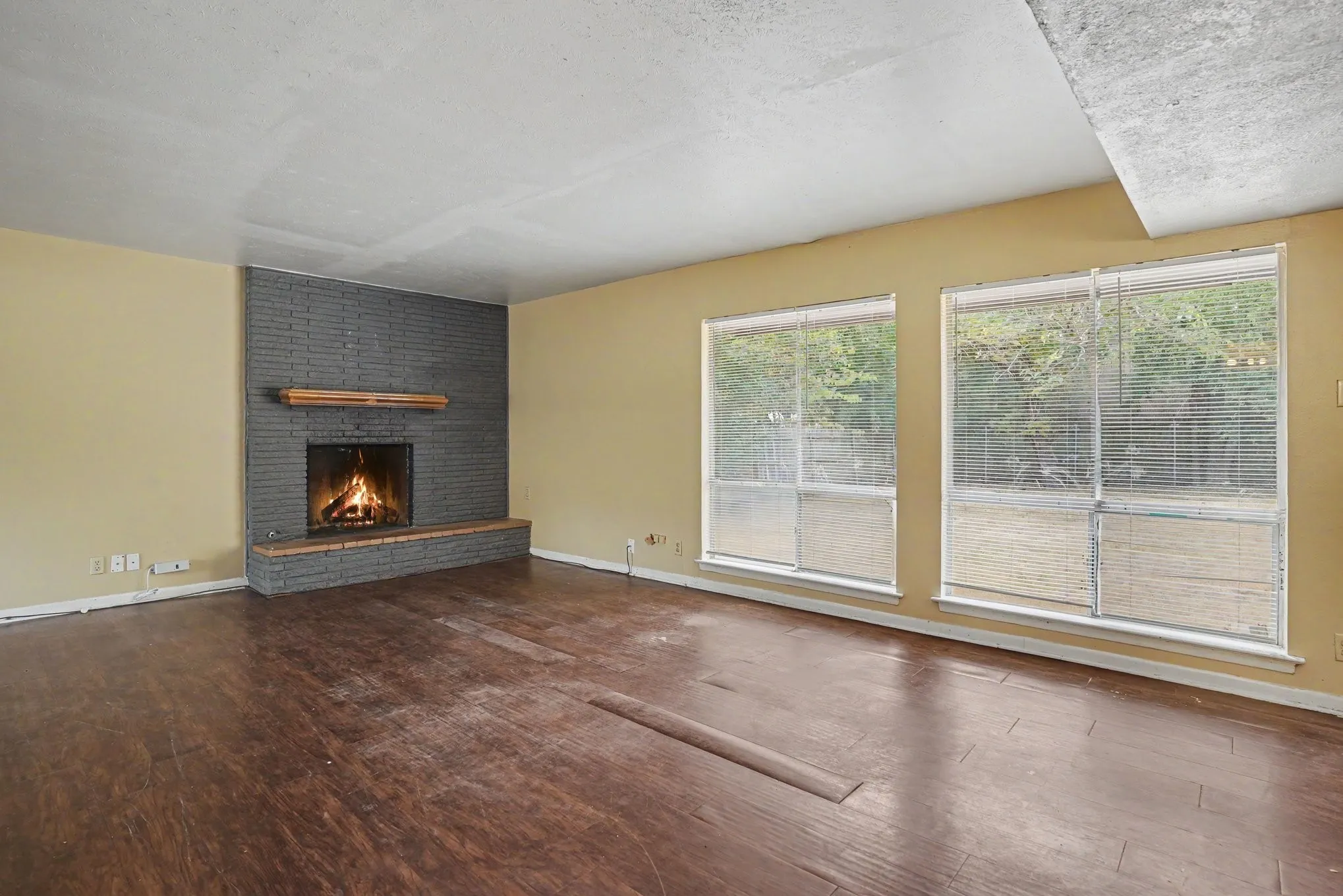 Spacious room featuring wood-finish flooring, a brick-surround fireplace with a wood mantle, and two large windows