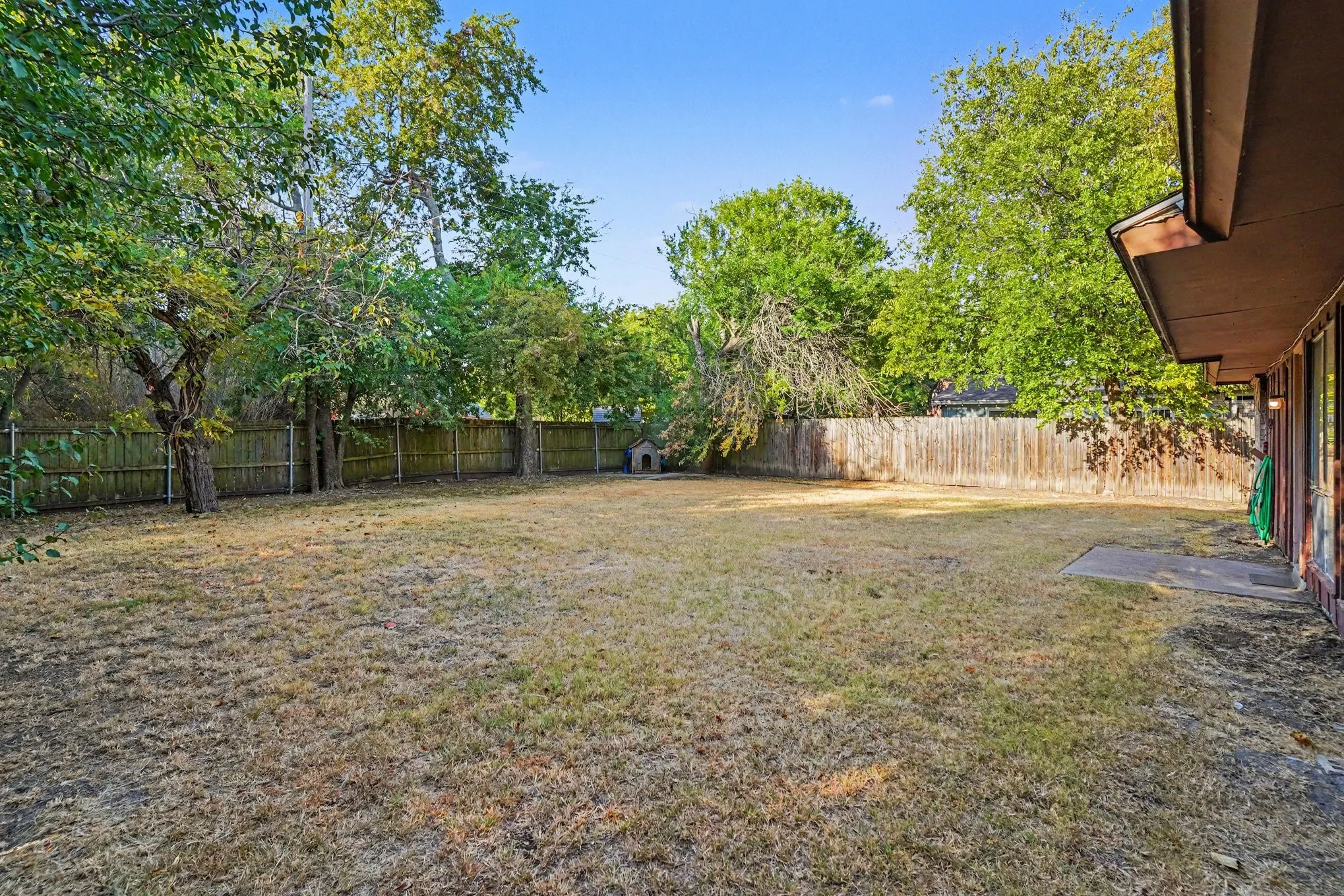 Expansive backyard featuring a wood fence, mature trees, and a concrete patio