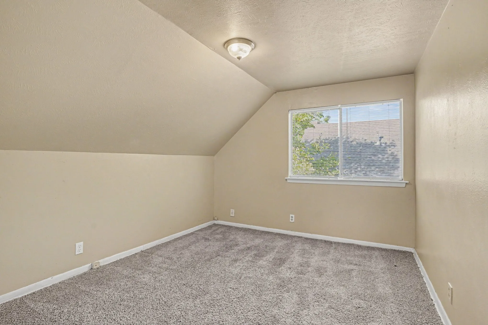 Sloped ceiling room featuring carpet flooring and a window with blinds