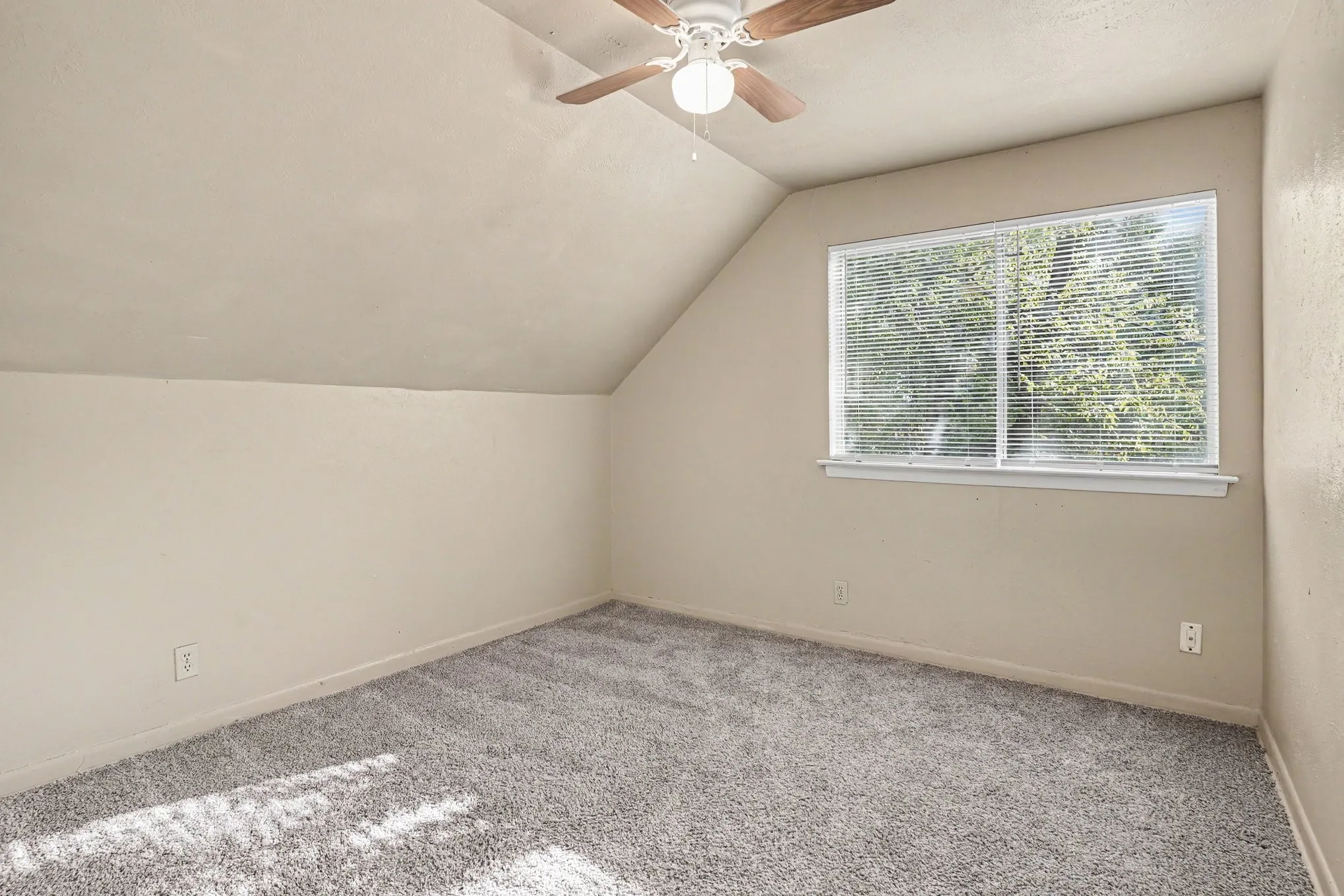 Sloped ceiling room featuring a ceiling fan, recessed window with blinds, and gray carpeting