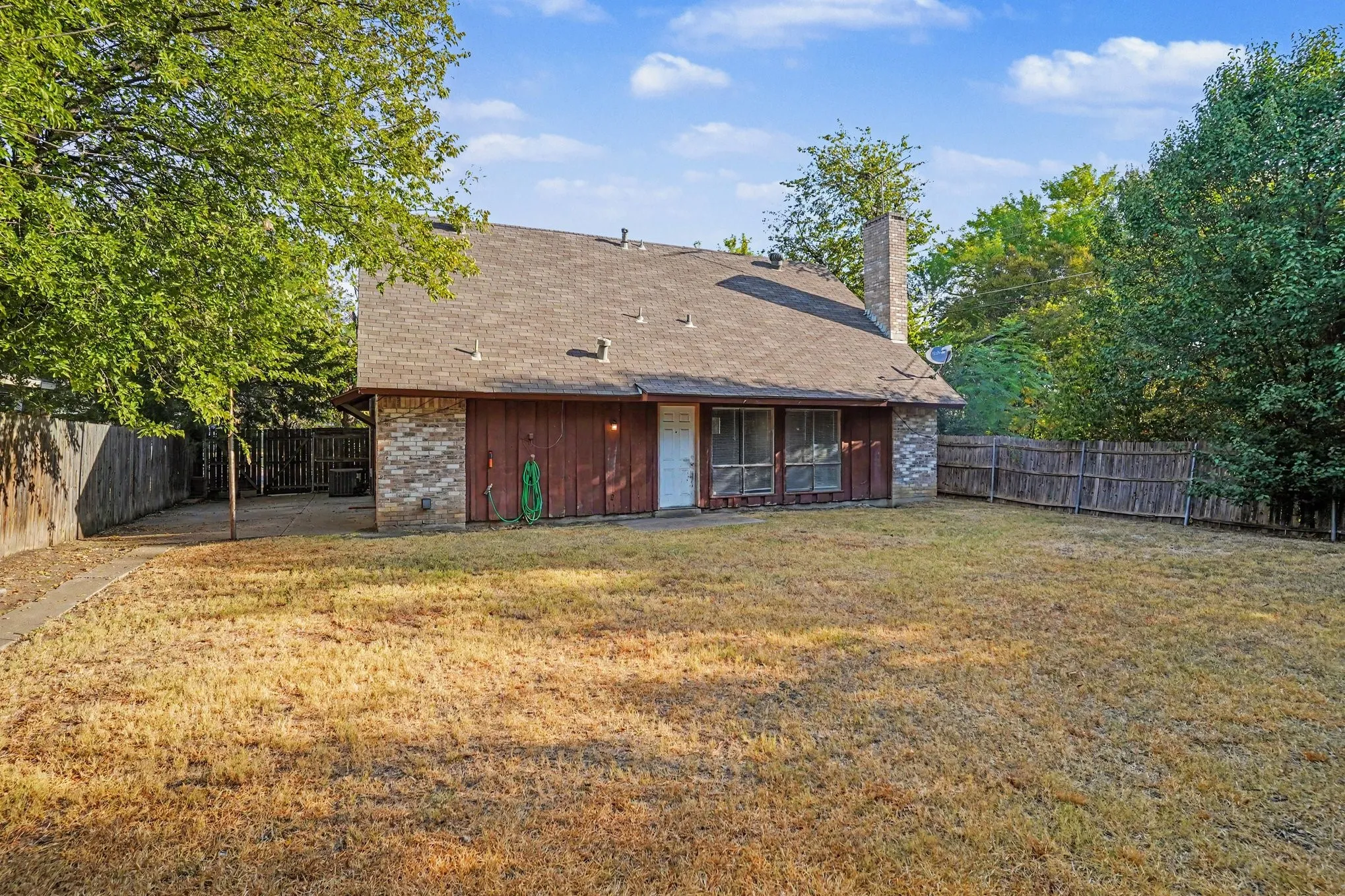 Expansive backyard featuring a partial brick and wood exterior, multiple mature trees, and a privacy fence