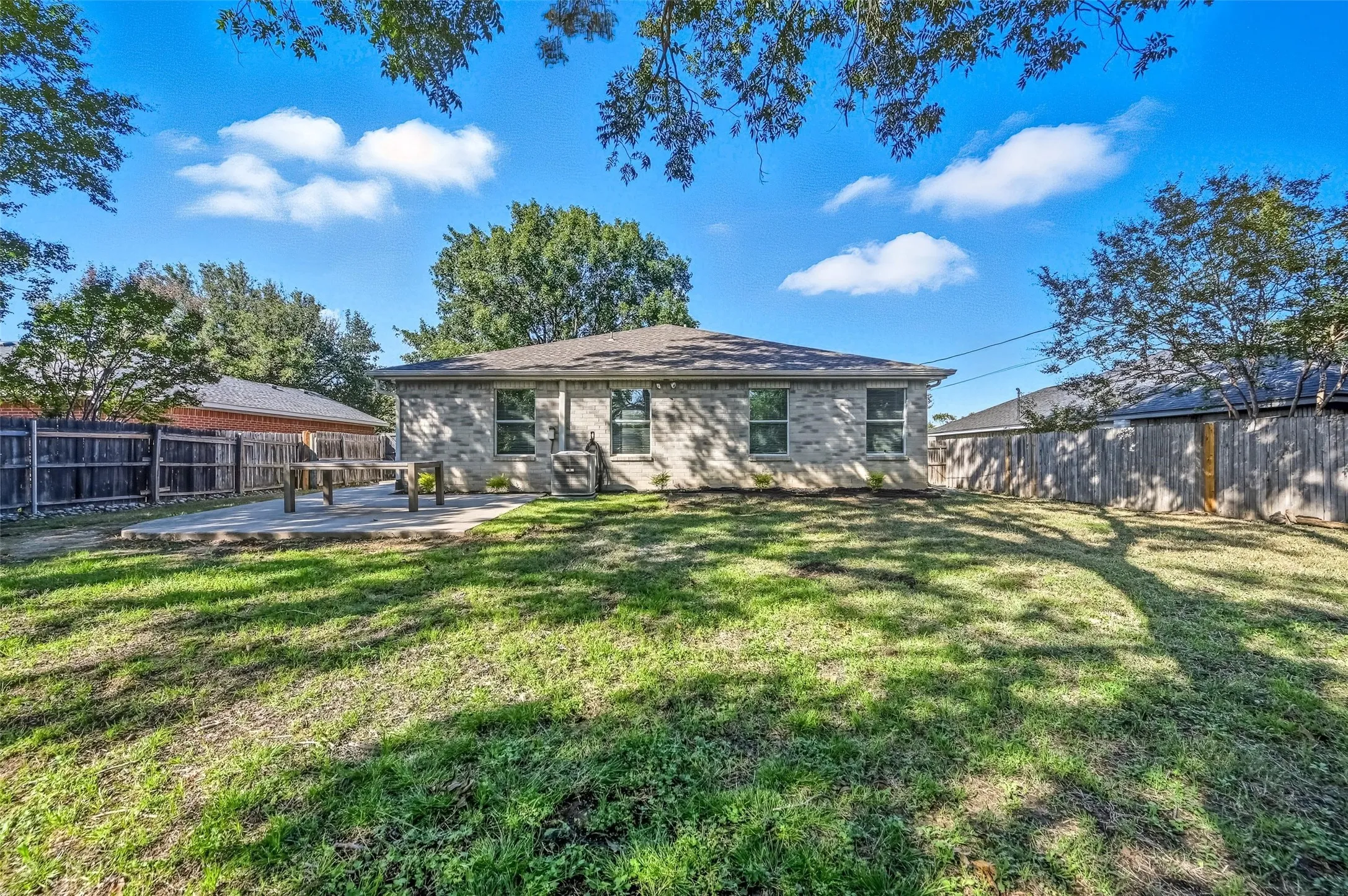 Large backyard with trees, concrete patio and newly installed sprinkler system.