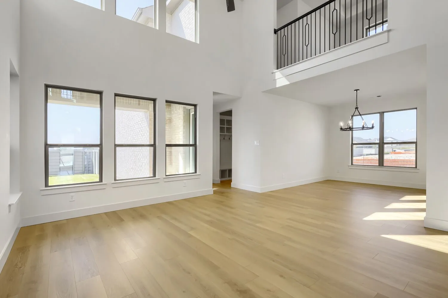 Expansive living area with wood-finish flooring, soaring ceilings, multi-pane windows, and a second-story interior balcony with wrought iron railing