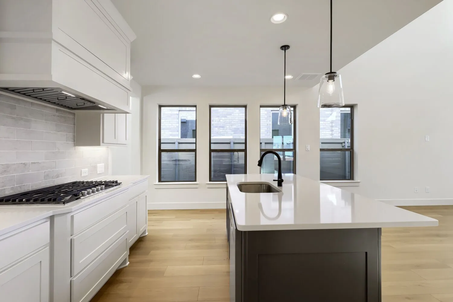 Spacious kitchen featuring an island with a built-in sink and faucet, white cabinetry, a gas range with a range hood, and light wood-finish flooring