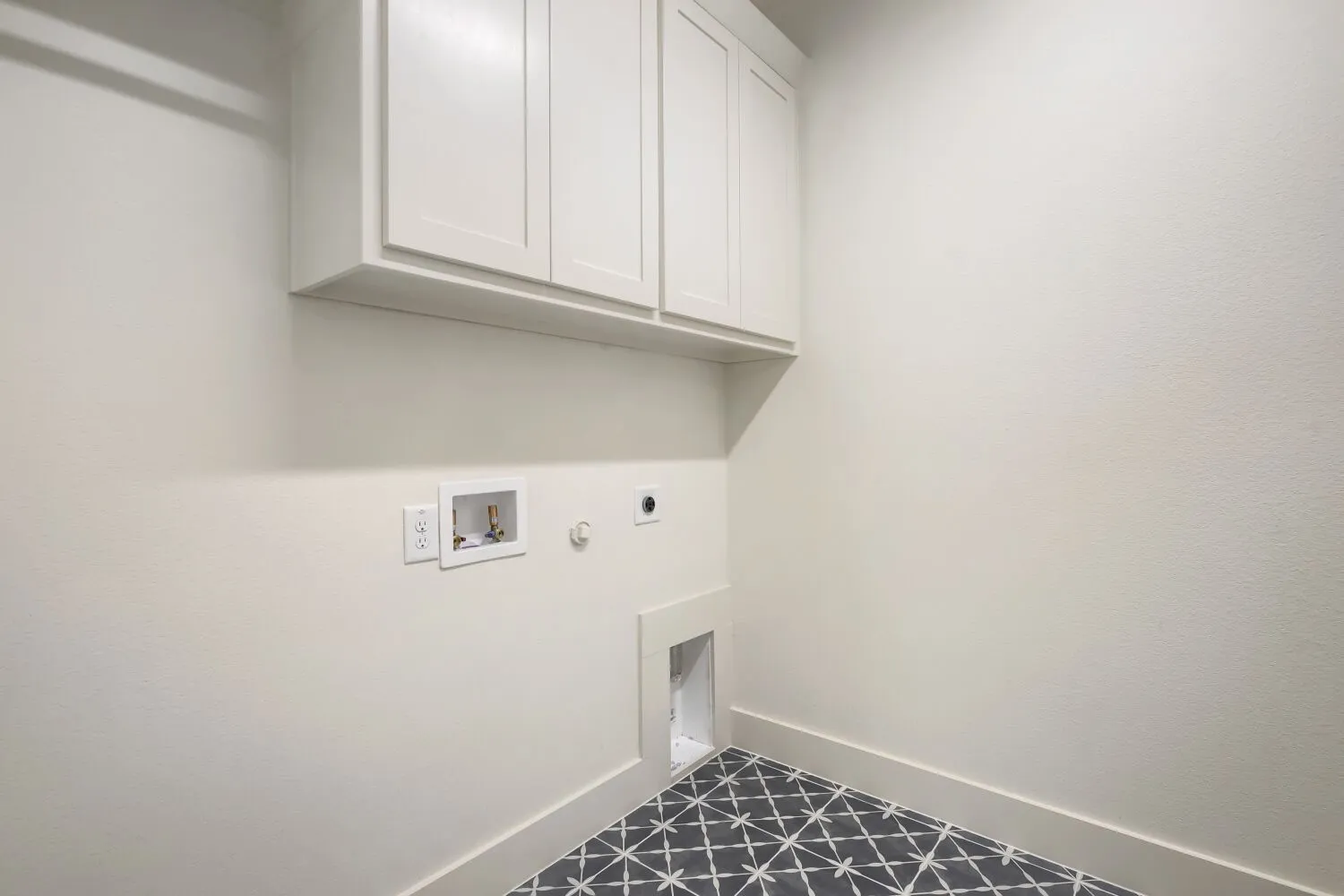Dedicated utility space featuring white cabinetry with ample storage, geometric patterned flooring, and convenient wall-mounted electrical outlets and switches for appliance connectivity
