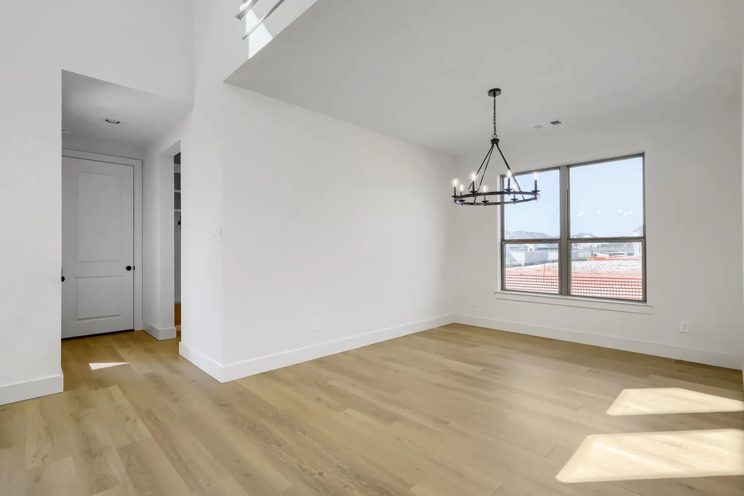 Wood-finish flooring throughout, complemented by a contemporary chandelier, large window, and high ceilings
