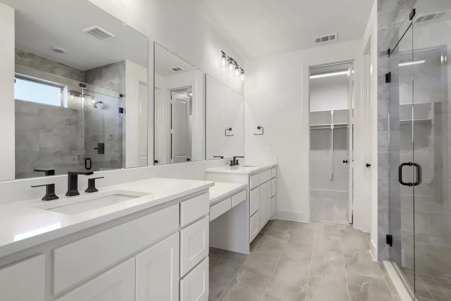 Dual vanity with matte black fixtures, full-width mirror, walk-in shower with glass enclosure, white cabinetry, and light-toned tile flooring