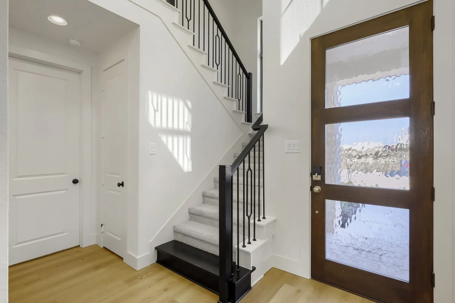 Wood-finish flooring, staircase with carpeted treads, wrought iron balusters, recessed lighting, and a front door with three rectangular frosted glass panels