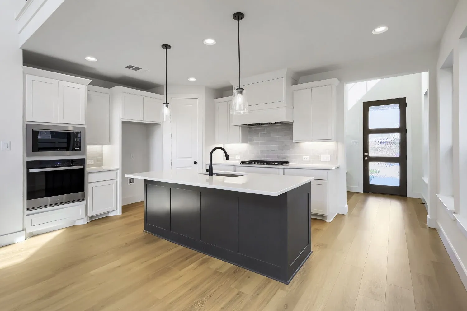 Kitchen featuring a dark-toned island with a white countertop, white cabinetry, integrated stainless steel appliances, and wood-finish flooring