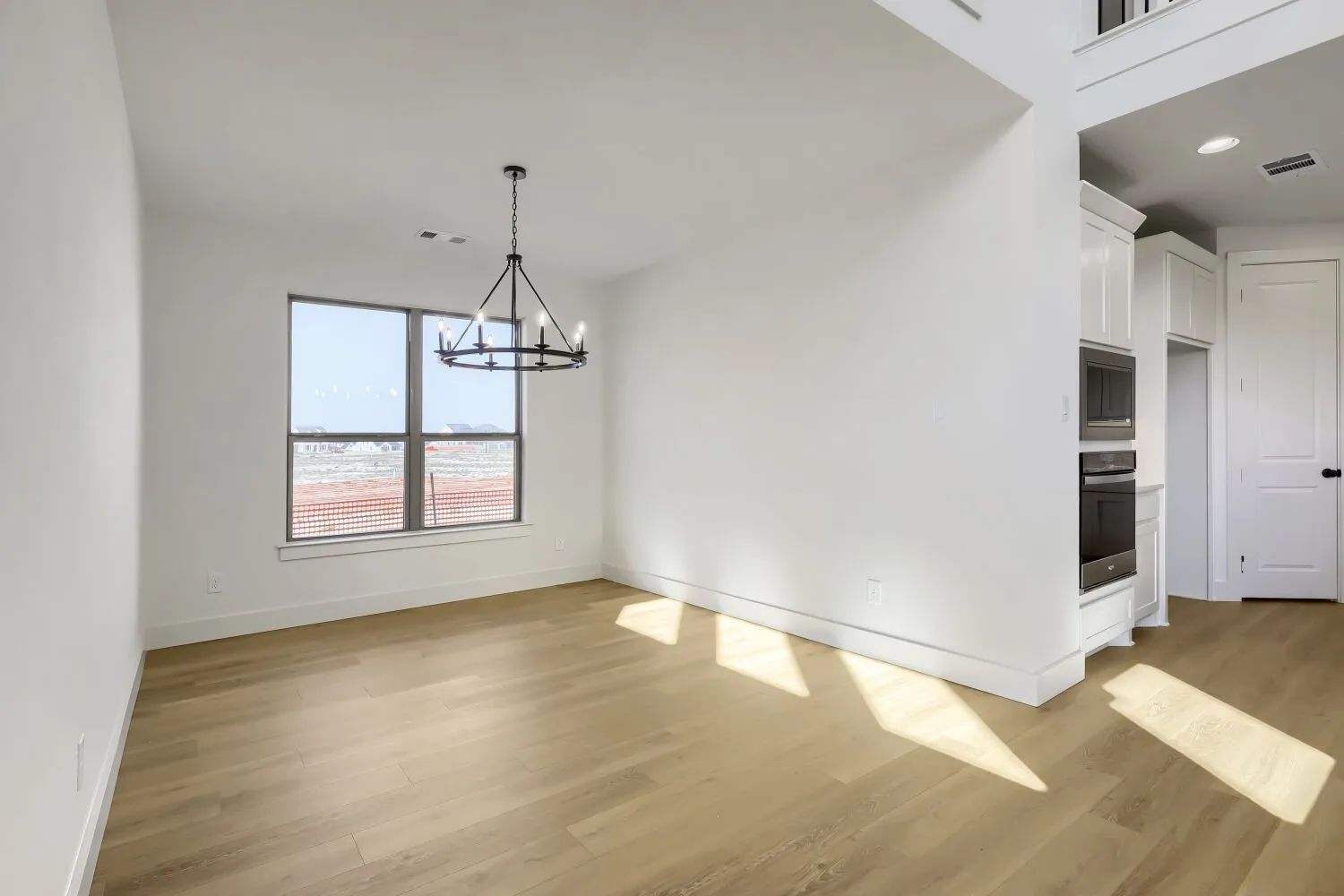 Spacious room with wood-finish flooring, a large window, and a contemporary chandelier